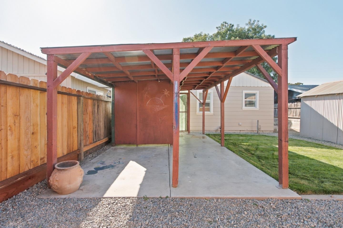 Backyard covered patio with a red timber frame, concrete slab, lawn, and wooden fencing.