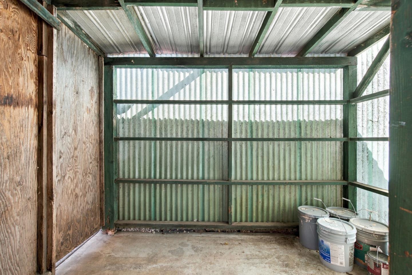 Utility shed interior with corrugated metal walls, green framing, and buckets on the concrete floor.
