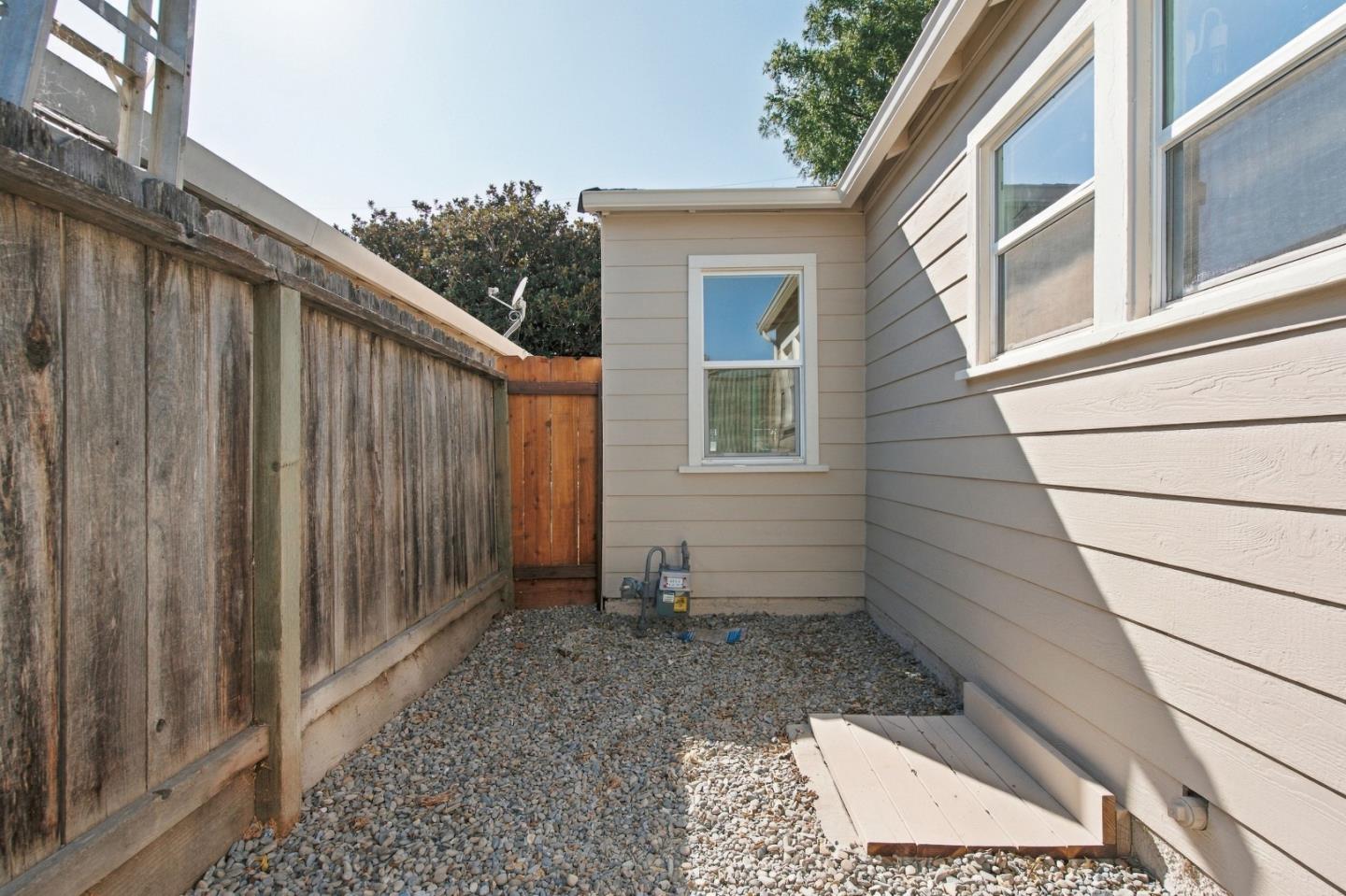 Gravel side yard between a light-sided house and a weathered wooden fence.