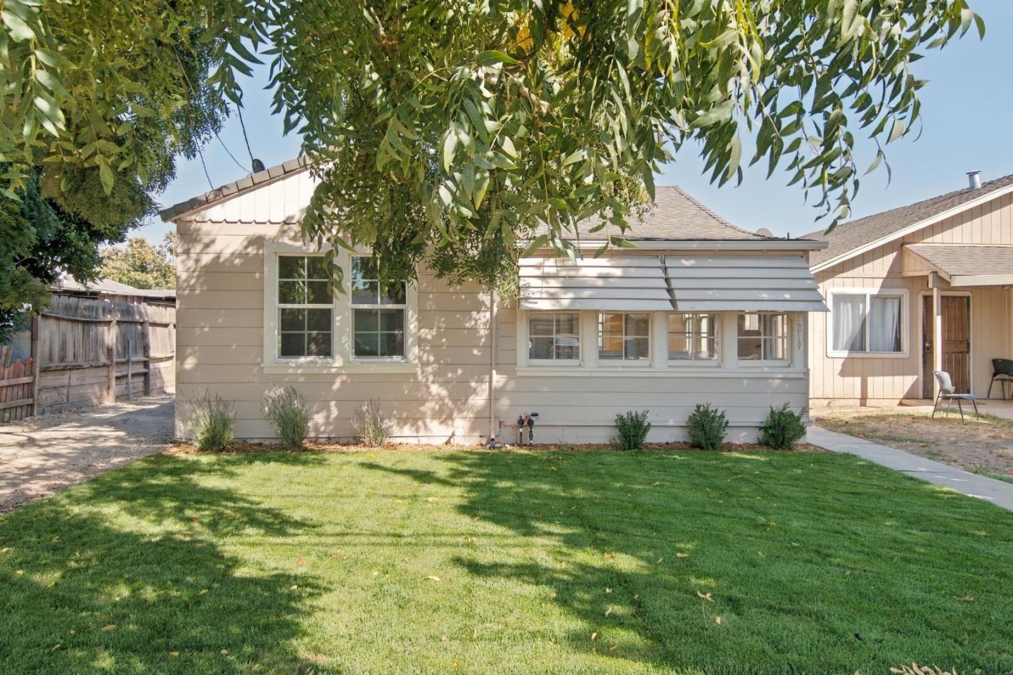Single-story home with an enclosed sunroom behind a broad lawn shaded by leafy branches.
