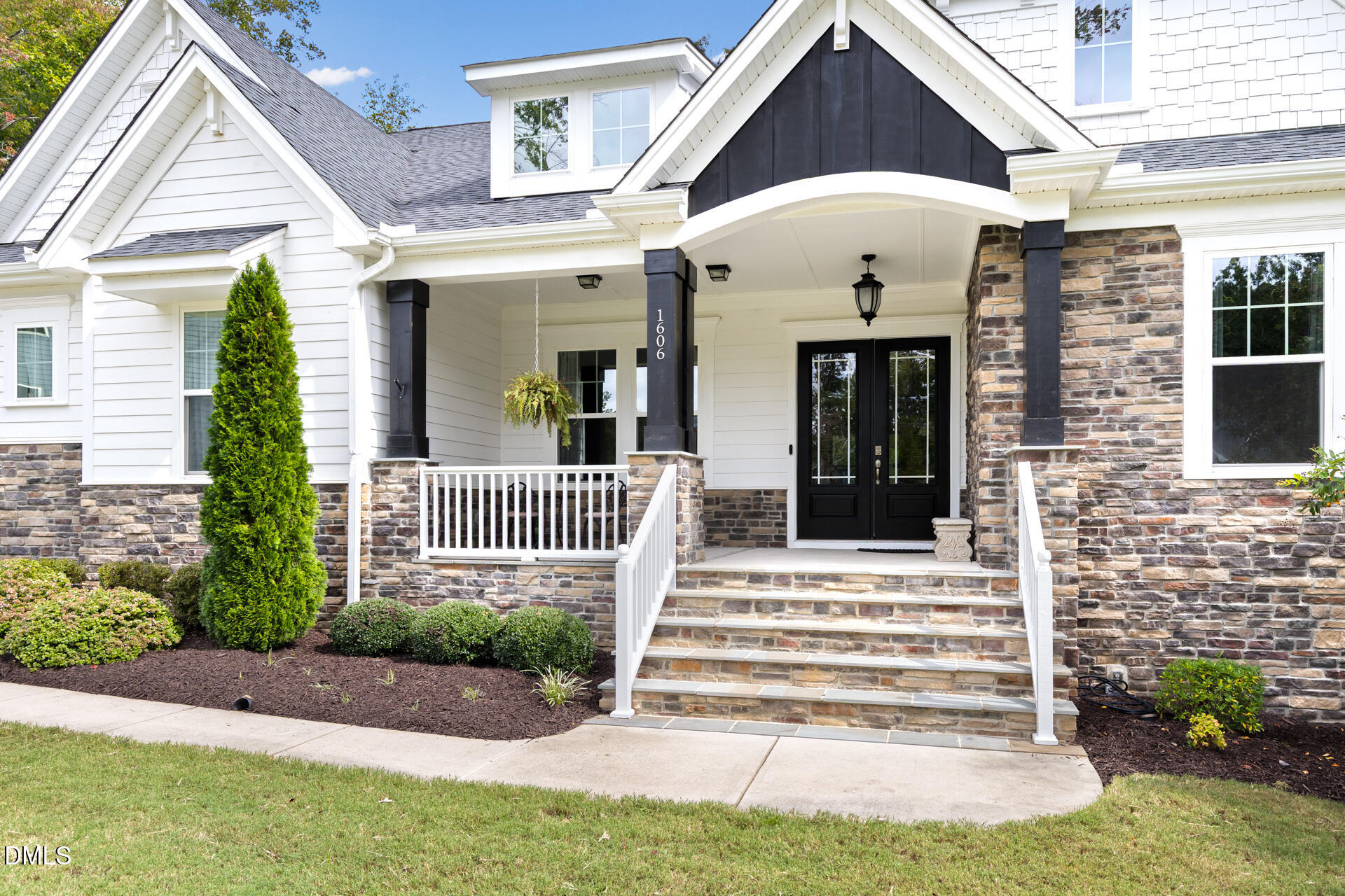 White two-story home with a covered porch, black double doors, stone steps, and landscaped entry.