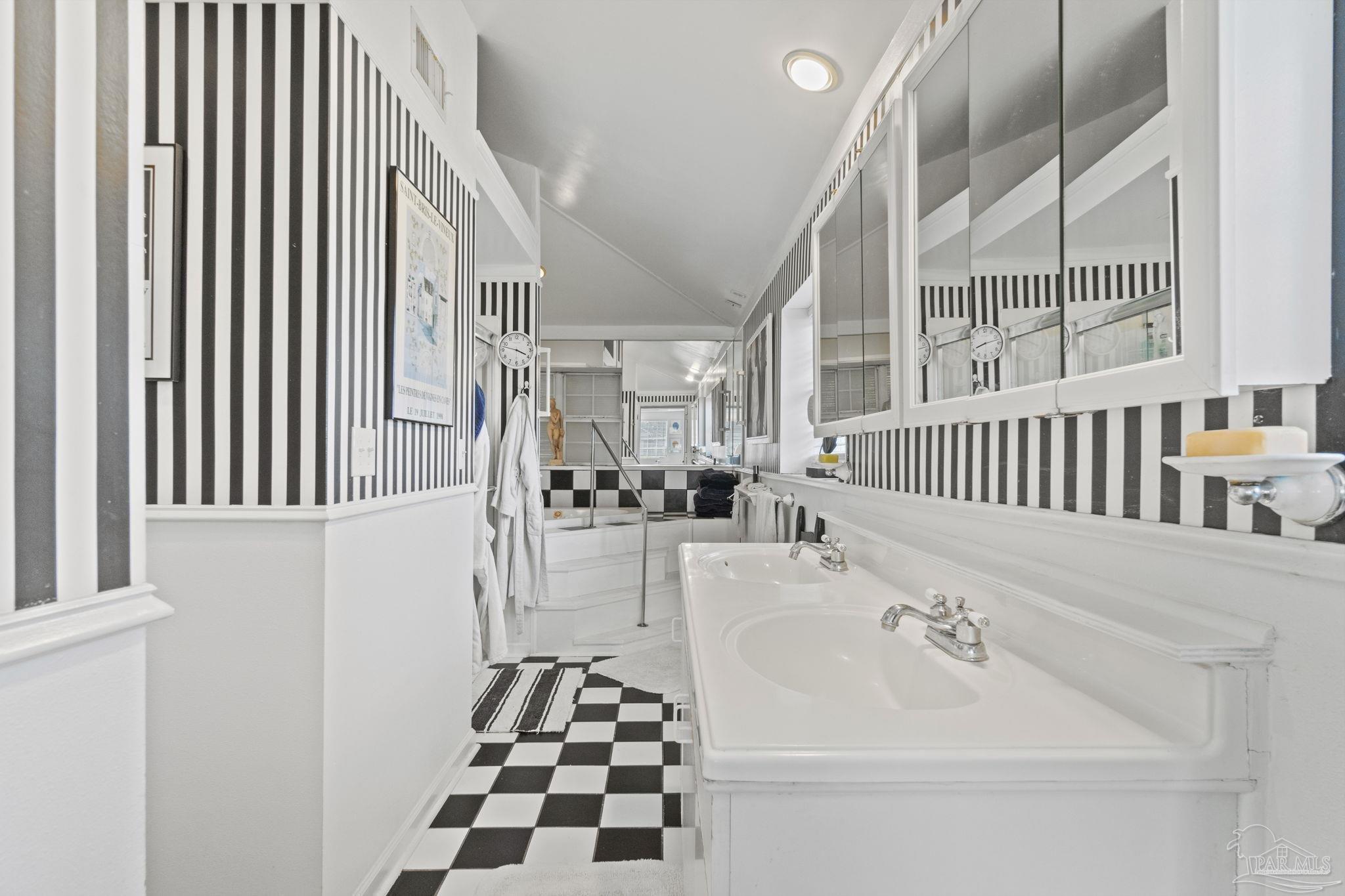 Bathroom with a long double-sink vanity, mirrored cabinets, and black-and-white checkerboard floors.