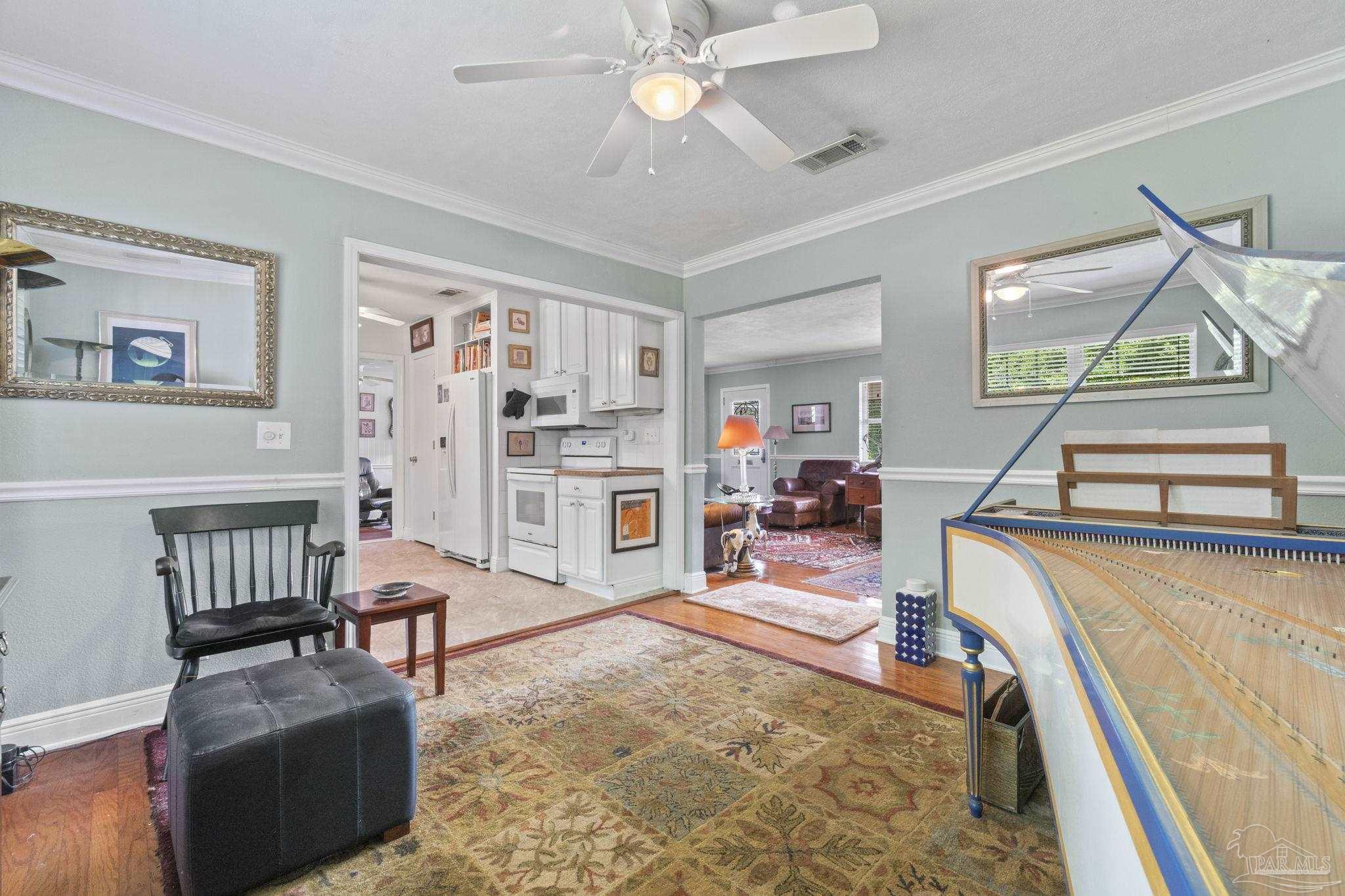 Furnished music room with a large keyboard instrument, patterned rug, and open views into the kitchen and living room.