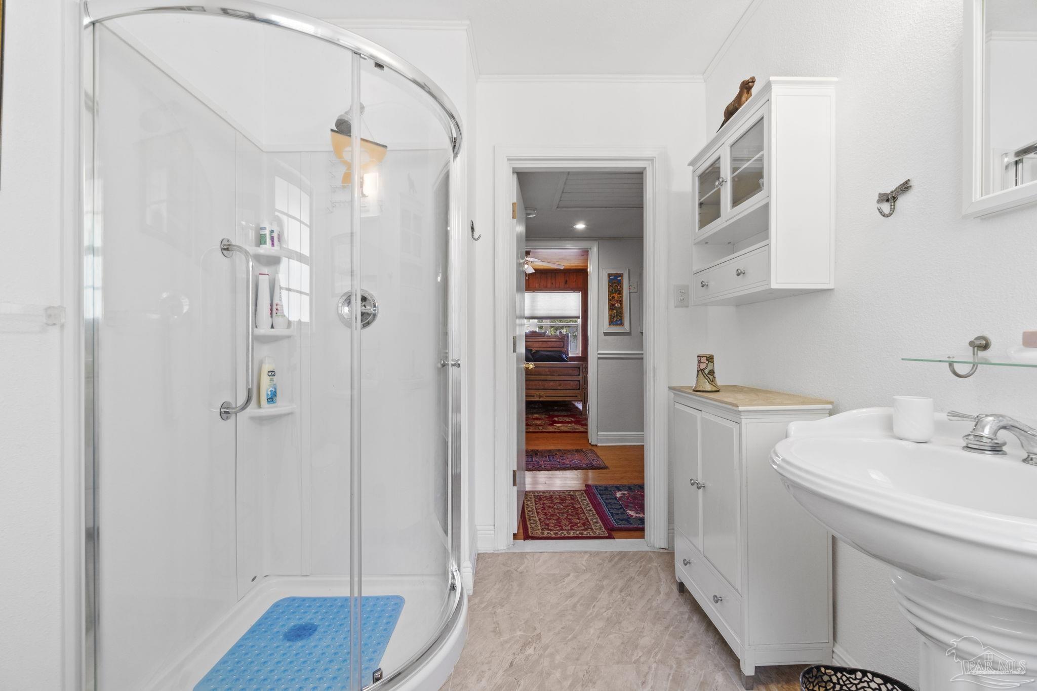 Bathroom with a curved glass shower and white vanity, looking through a doorway to a wood-floored room.