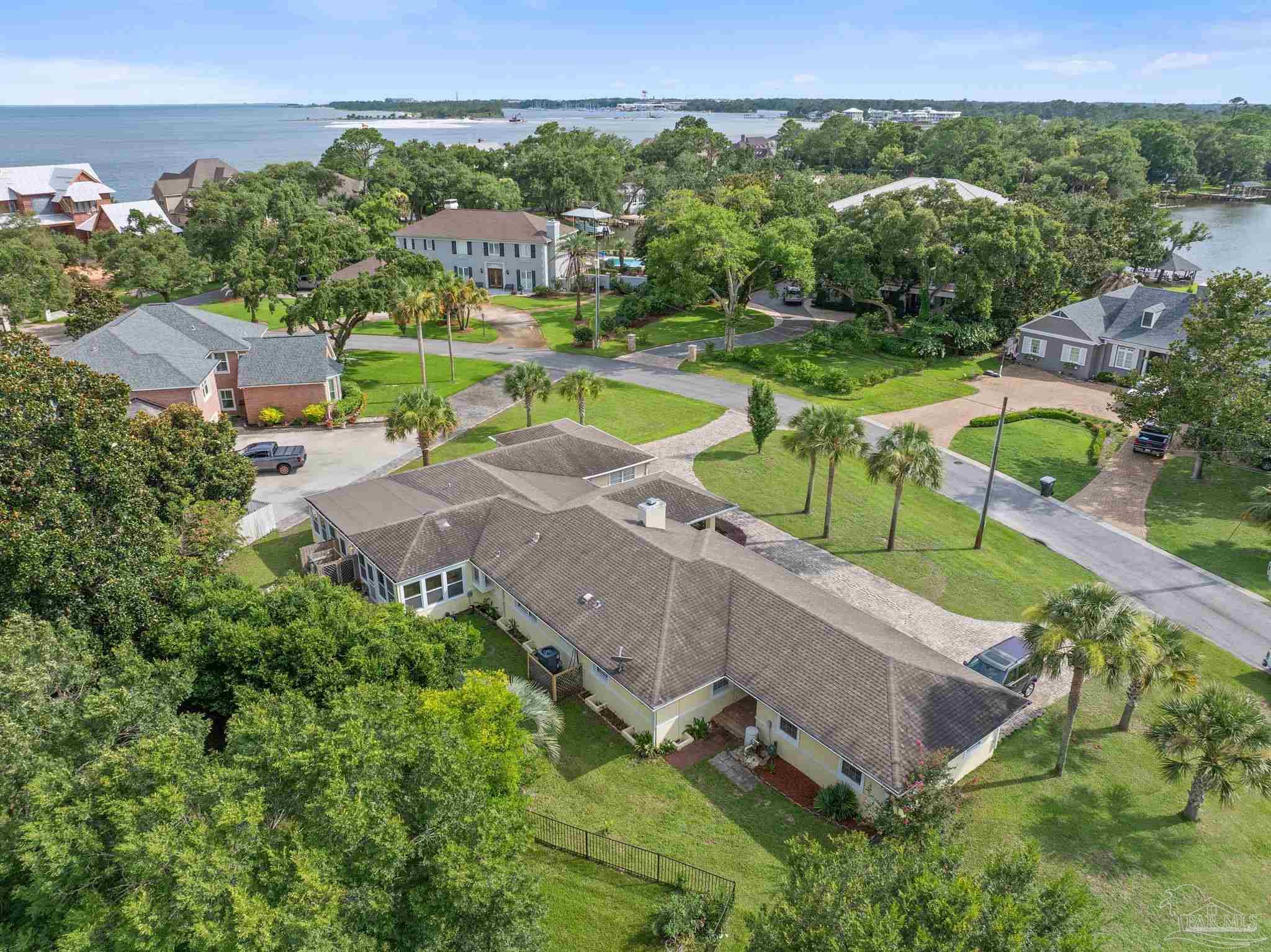 Aerial view of a single-story home near the waterfront, with the bay and neighboring homes beyond.