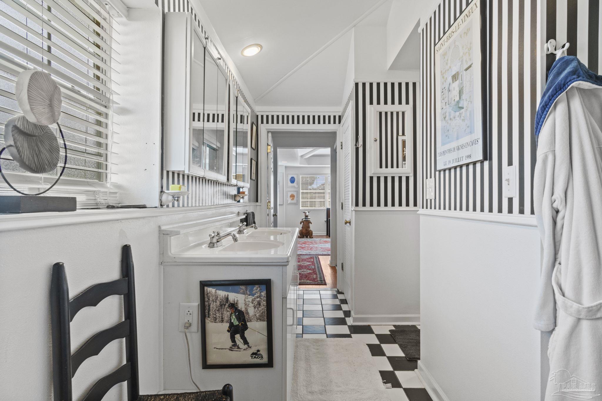 Bathroom with a double-sink vanity, striped wallpaper, and checkerboard floor.