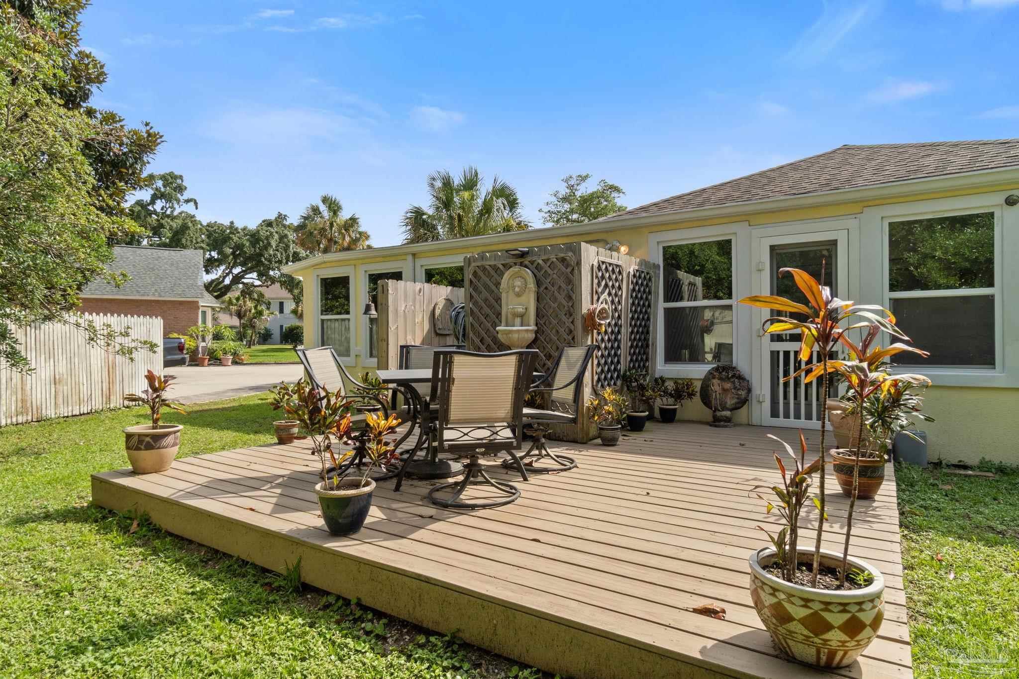 Wooden deck with patio dining set, potted tropical plants, and a lattice fountain screen beside the house.