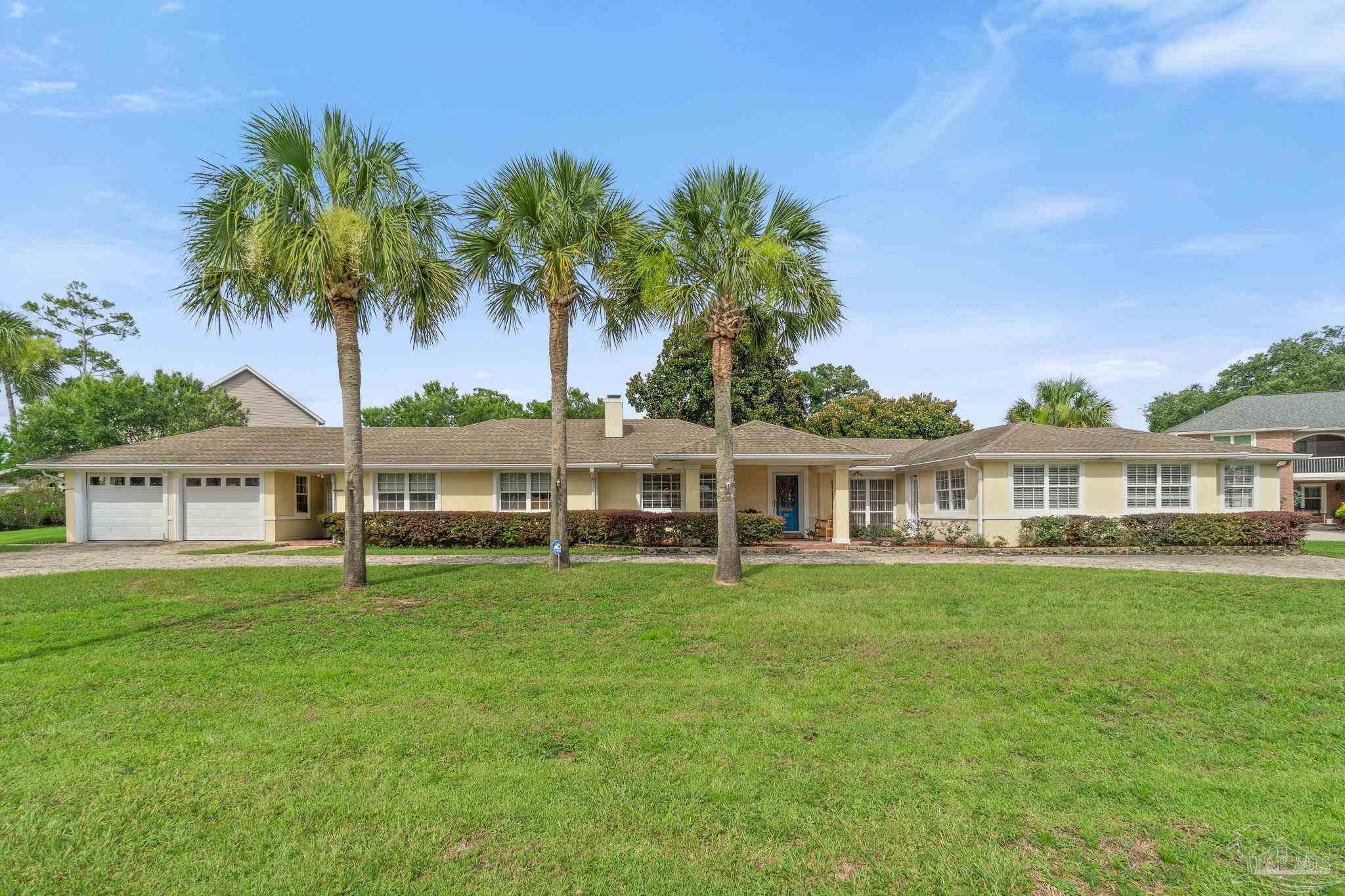 Single-story beige home with a two-car garage, blue front door, and tall palms across the lawn.