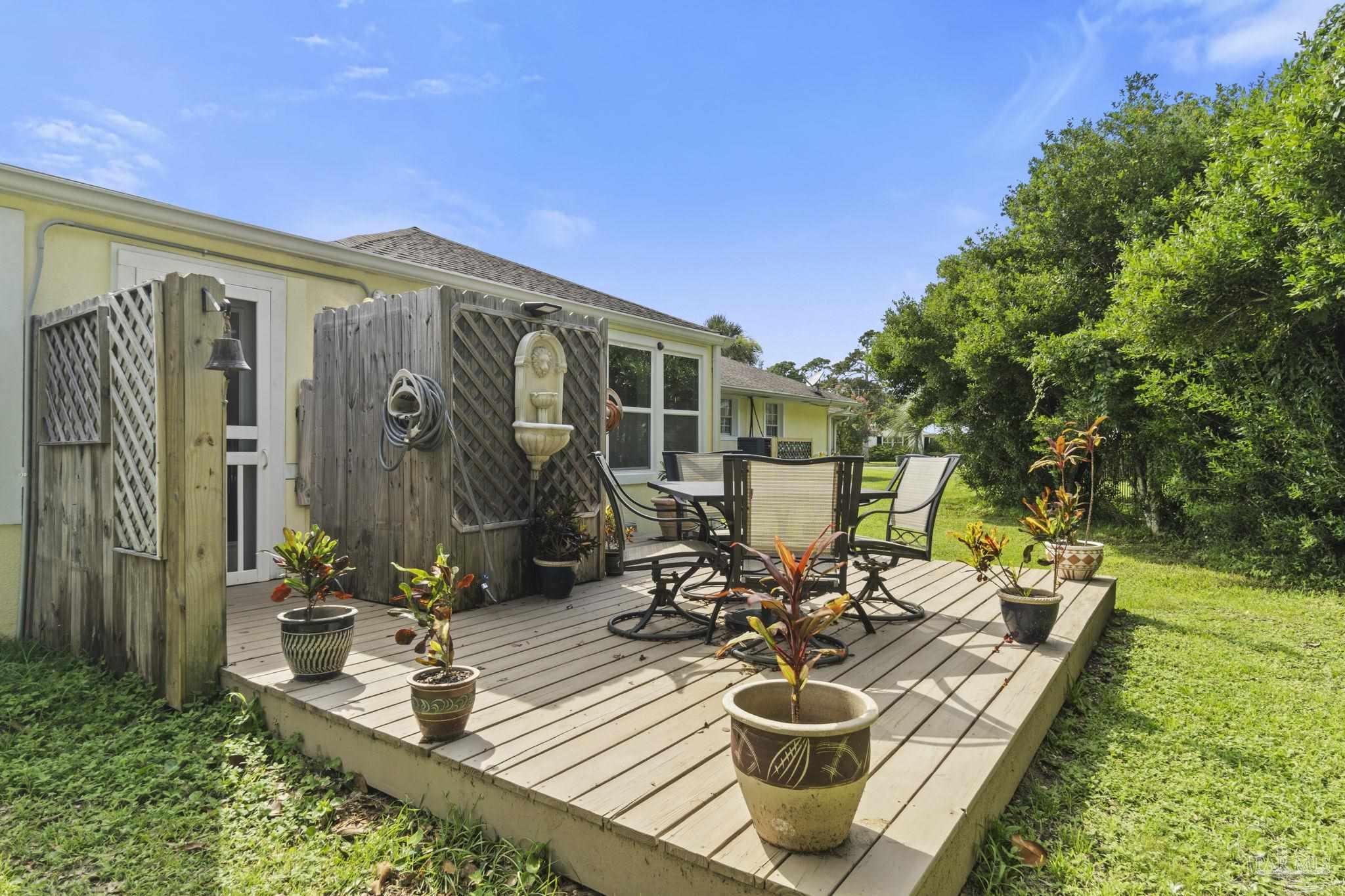 Wooden deck with patio seating, potted plants, and a wall fountain beside the home.