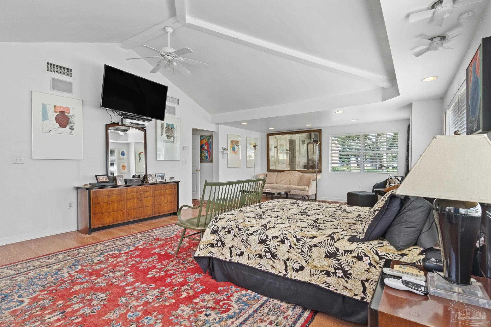 Bedroom with vaulted ceiling, floral bedspread, red patterned rug, and a sitting area.