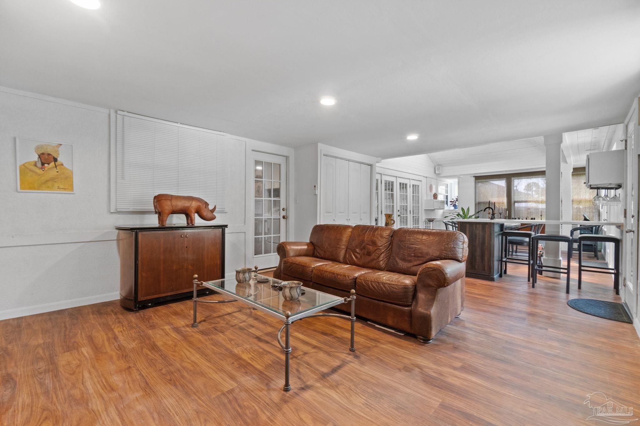 Open-plan living room with brown leather sofa and wood floors, adjoining a kitchen with a bar island.