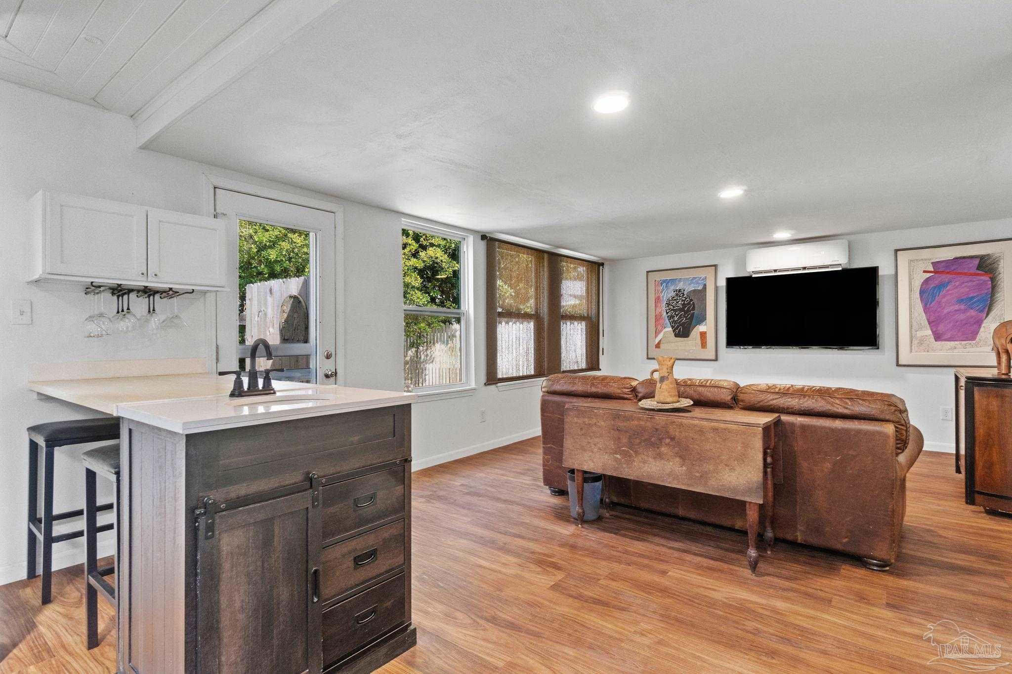 Open-plan living room and kitchen with a dark wood island and brown leather sectional.