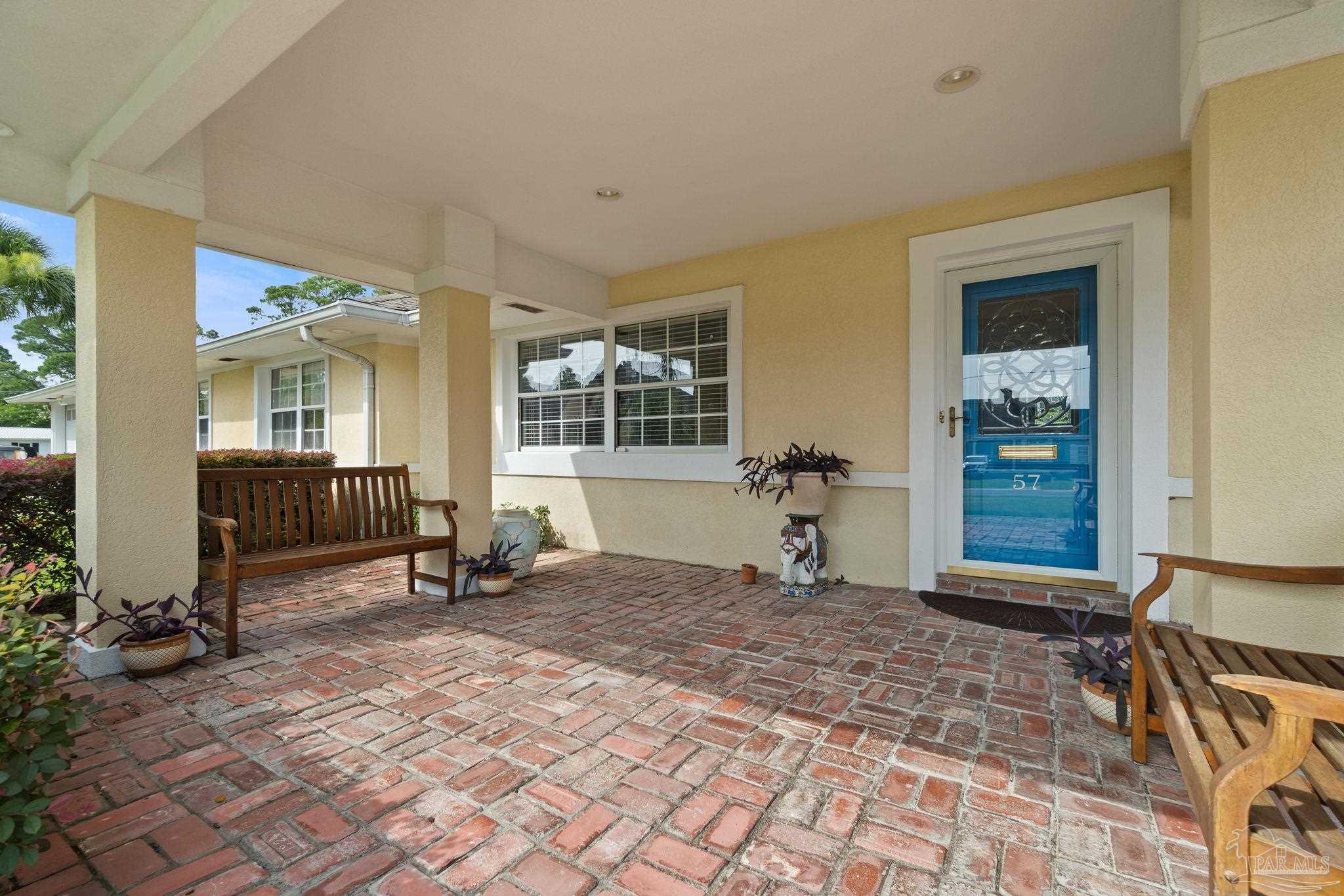 Covered front porch with brick pavers, wooden benches, and a blue front door.
