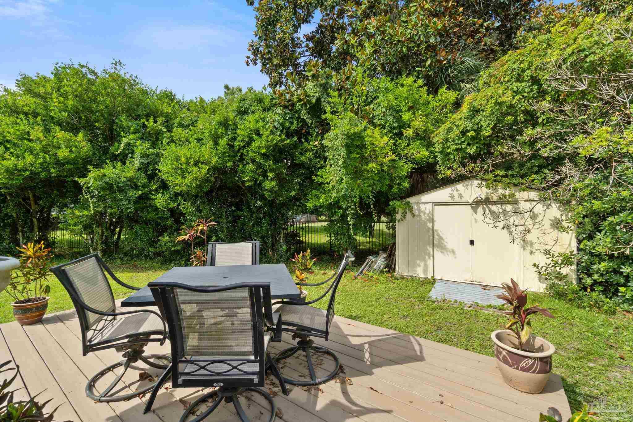 Outdoor deck with a patio dining set overlooking a leafy backyard and storage shed.