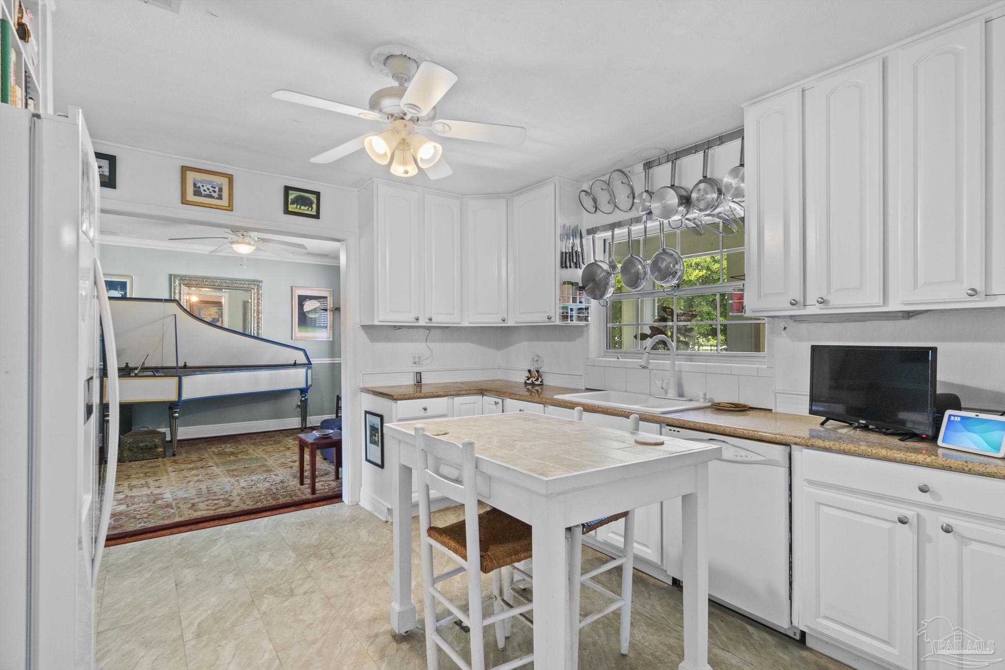 White kitchen with a tiled island, hanging cookware, and an adjoining room with a game table.