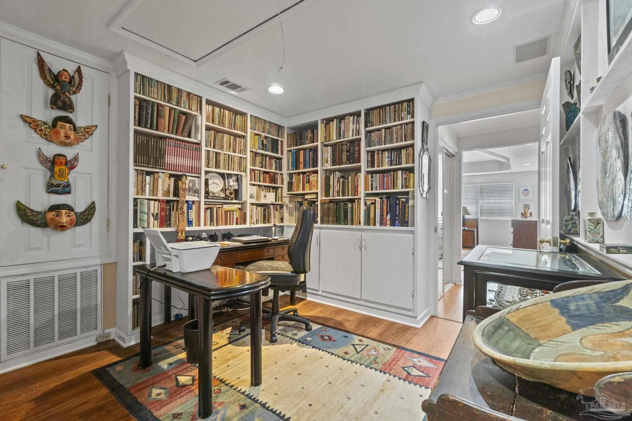 Home office lined with built-in bookshelves, featuring a desk, colorful rugs, and display cabinets.