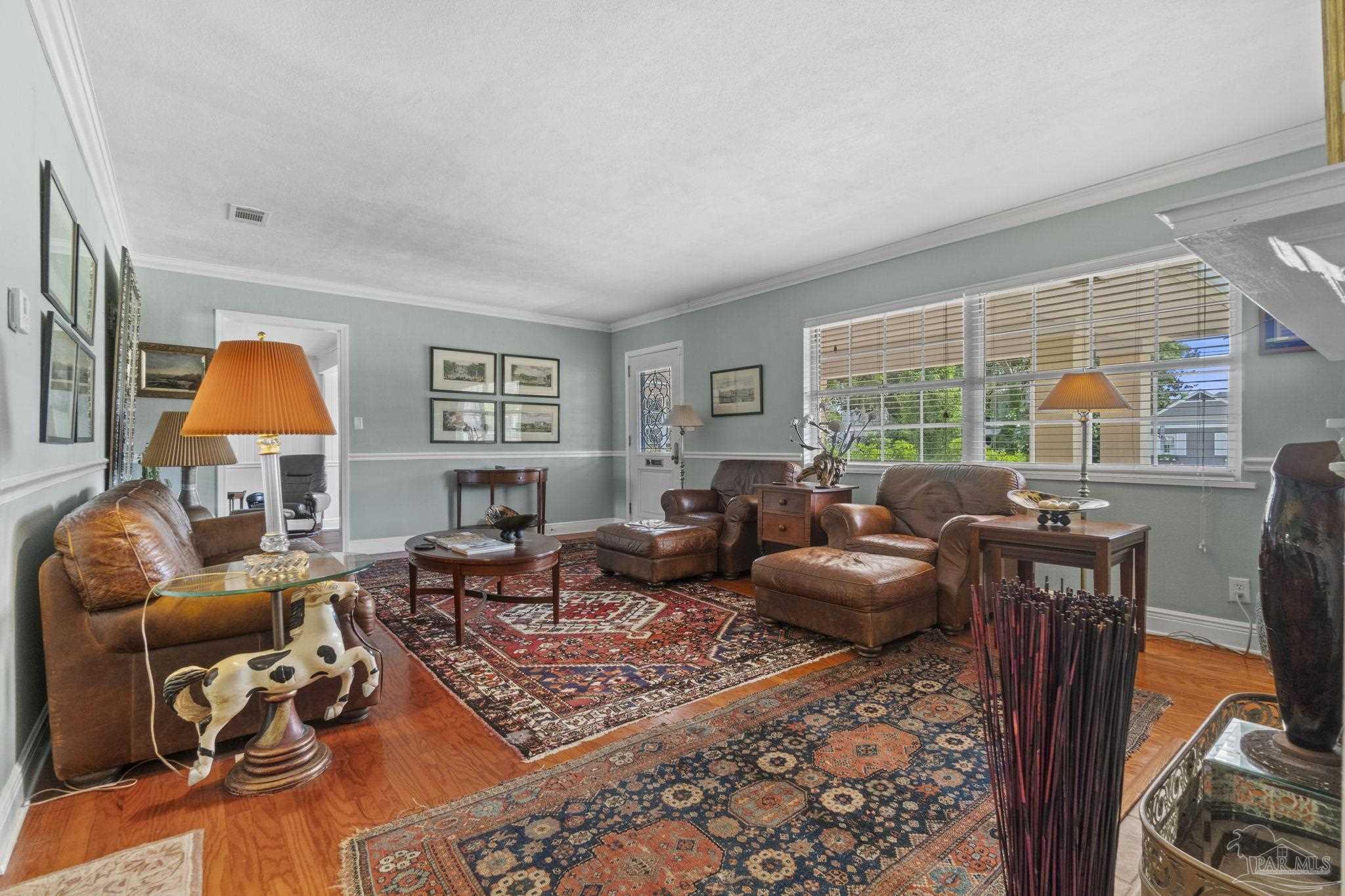 Living room with brown leather seating, layered patterned rugs, and a wide window with blinds.