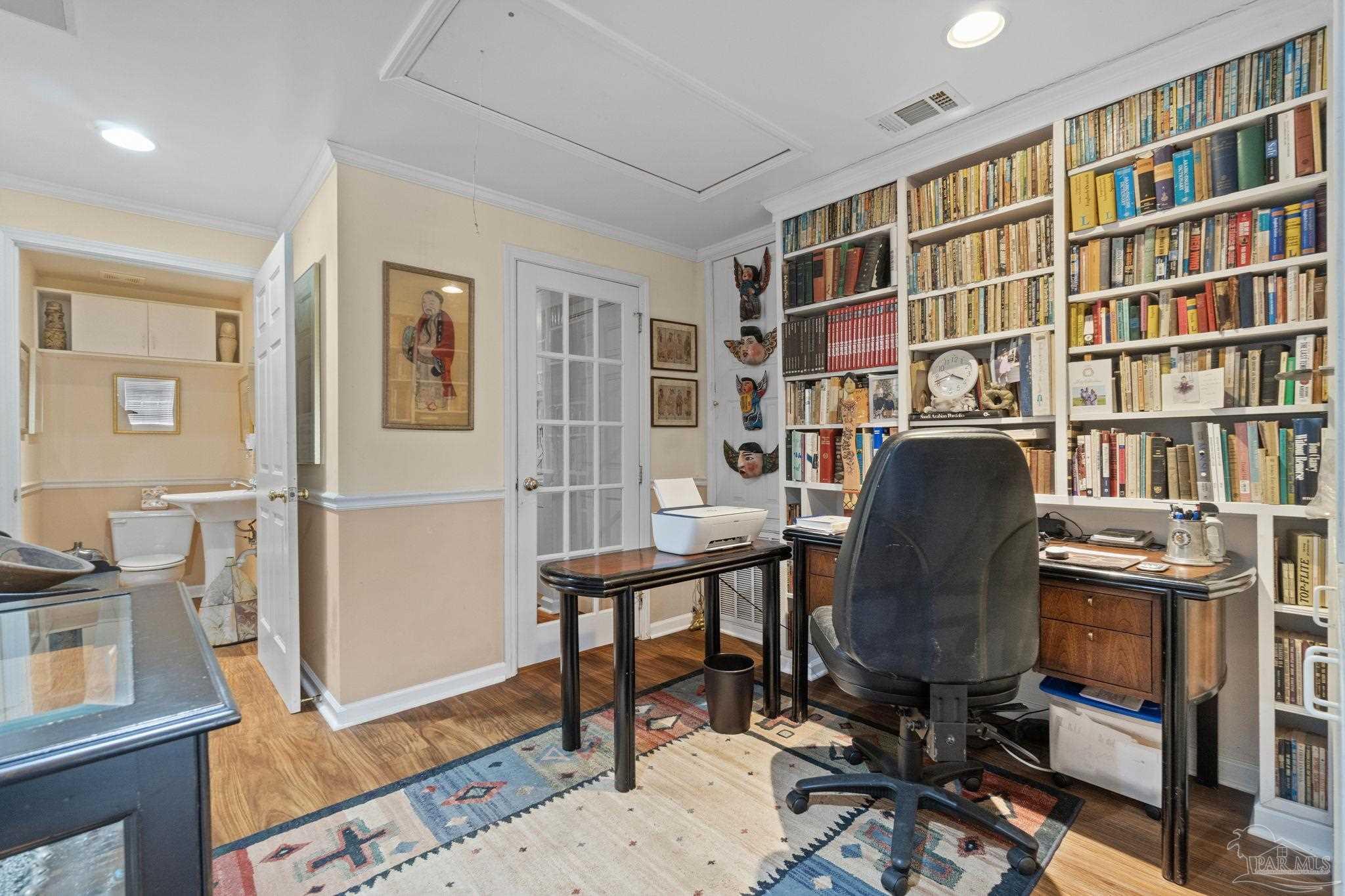 Home office with wall-to-wall bookshelves, a wooden desk, and an adjoining bathroom.