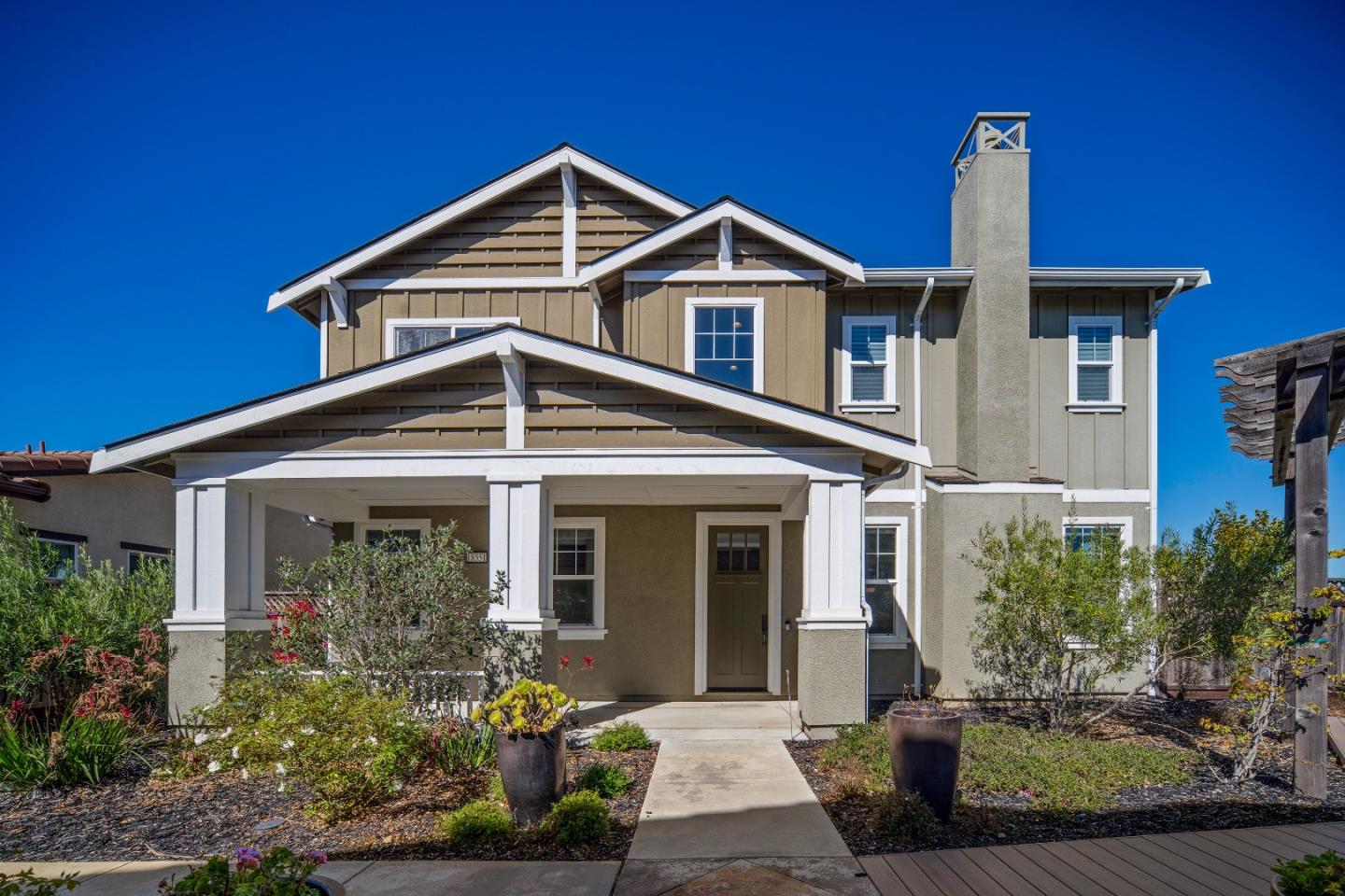 Two-story beige home with white-trimmed gables, a covered entry, and landscaped front yard.