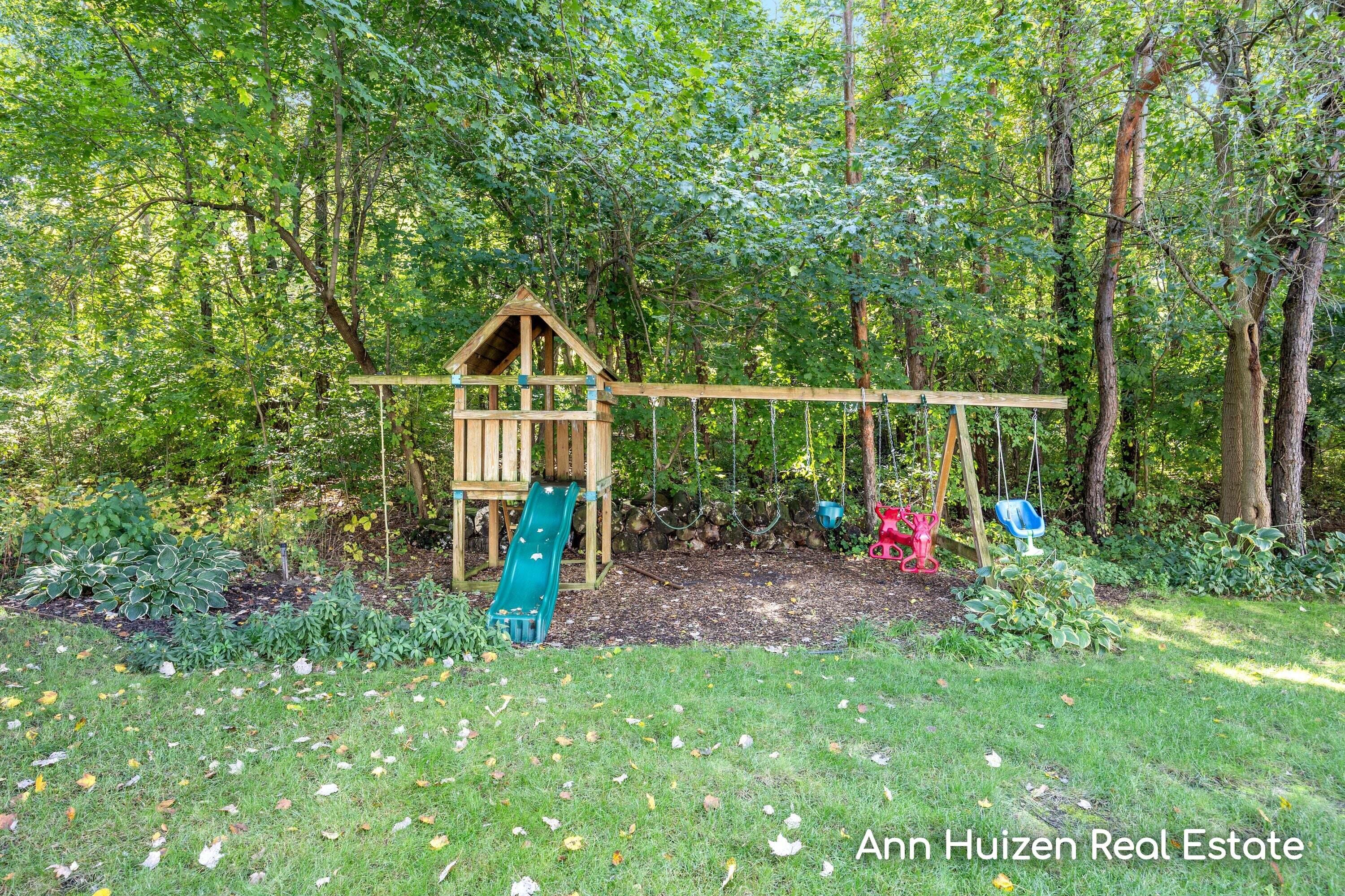 Backyard playset with a teal slide and several swings beneath mature trees.