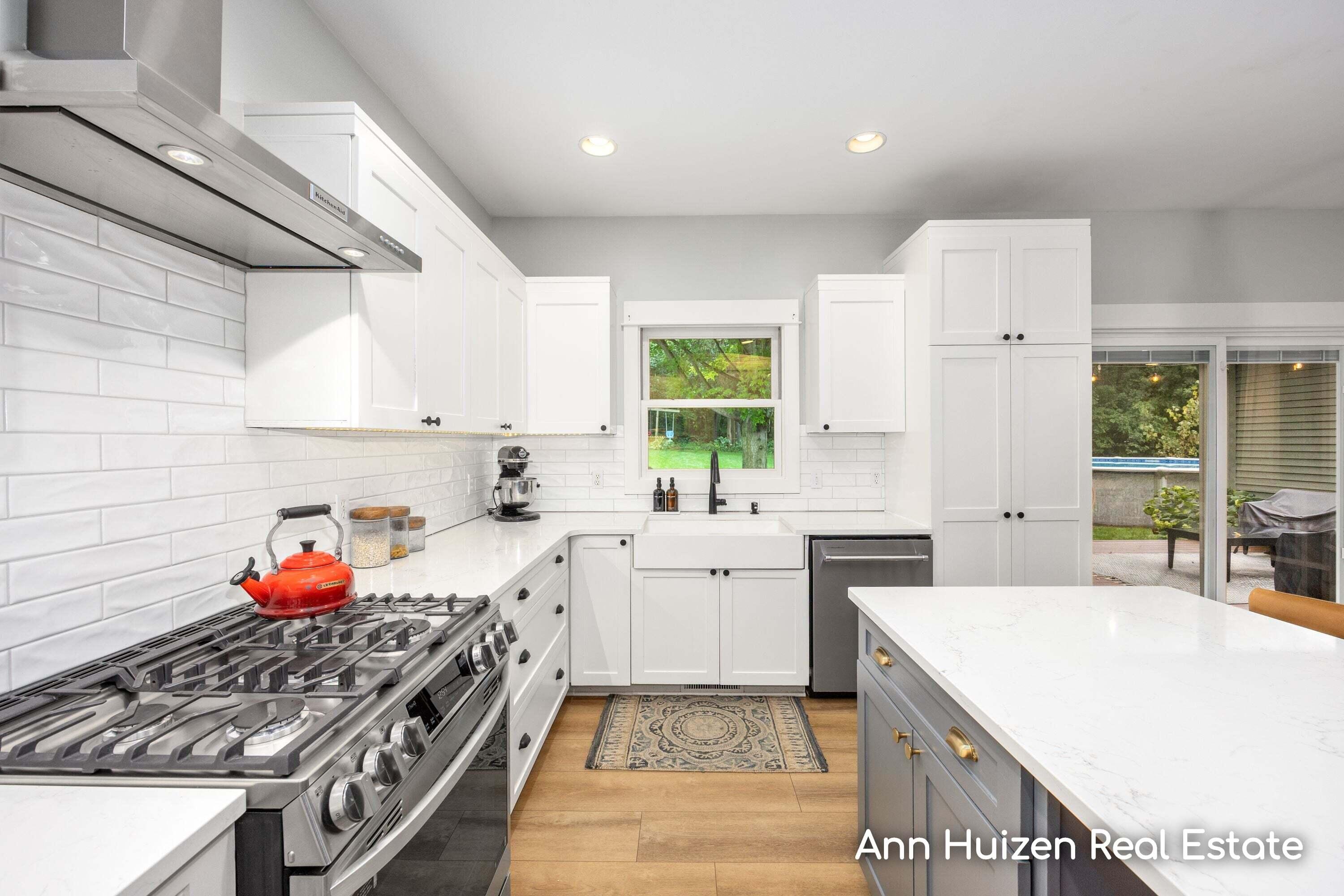 Bright white kitchen with quartz island, stainless gas range, and window overlooking the yard.