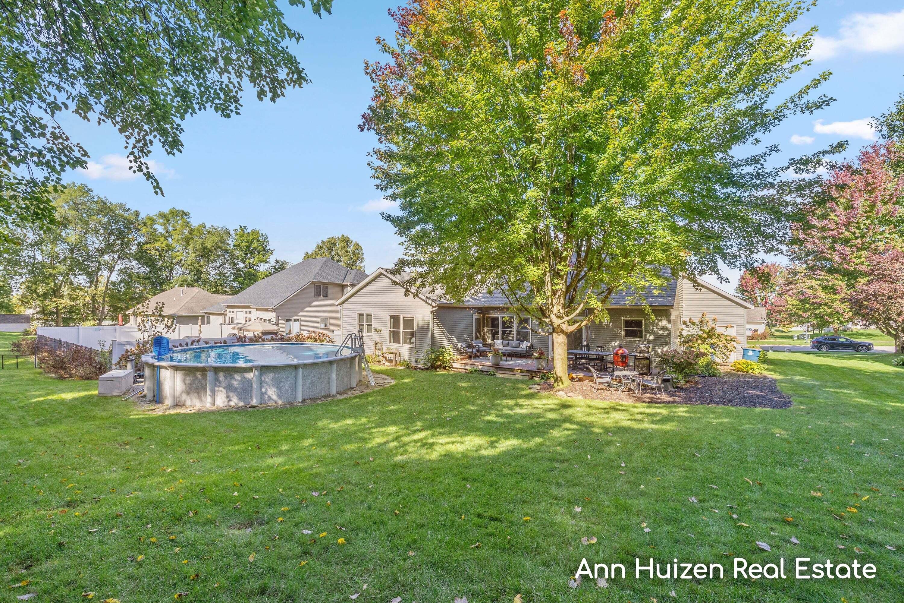 House backyard with a large shade tree, patio seating, and an above-ground pool.
