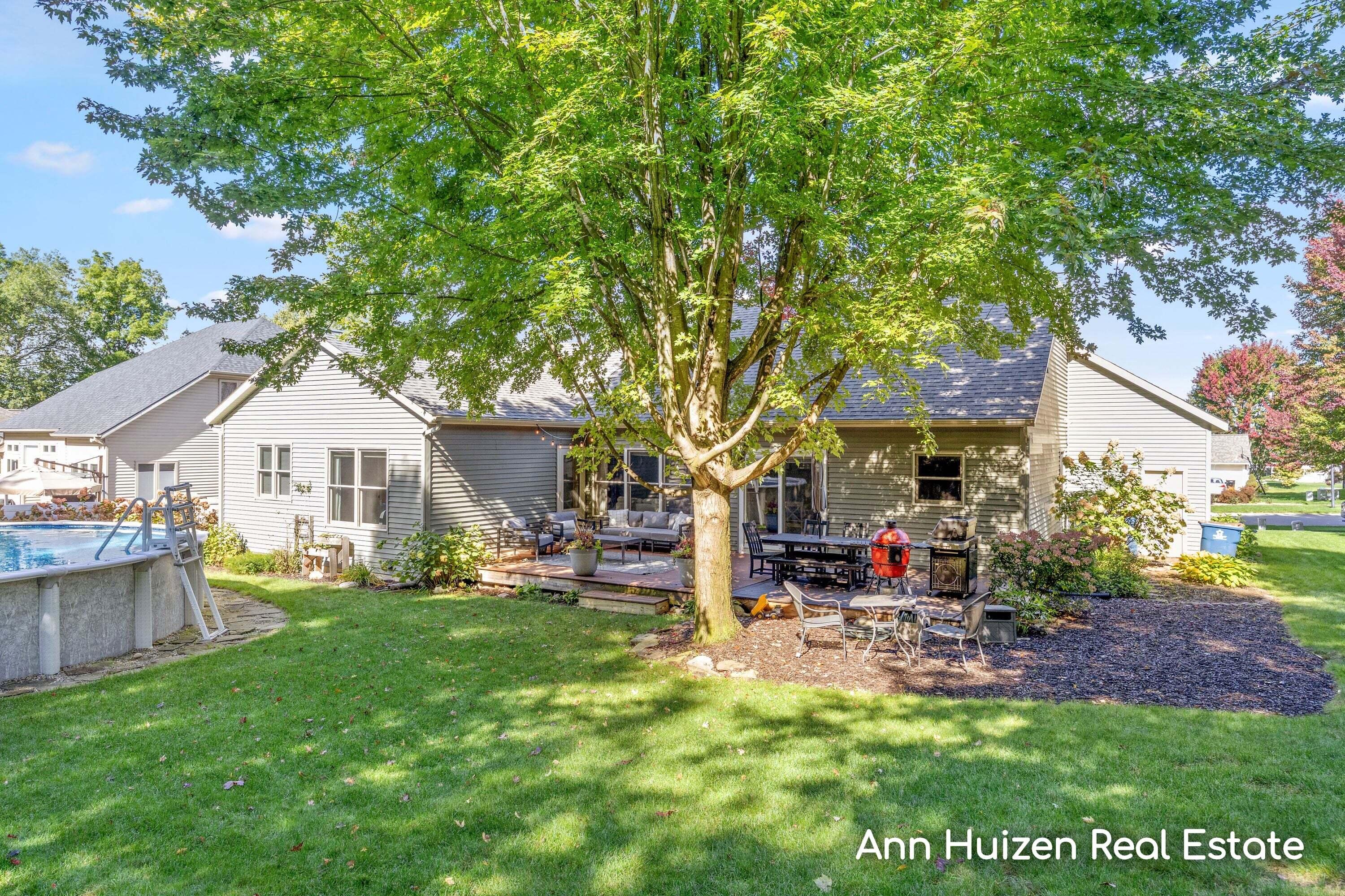 House rear with a furnished deck, large shade tree, and above-ground pool.