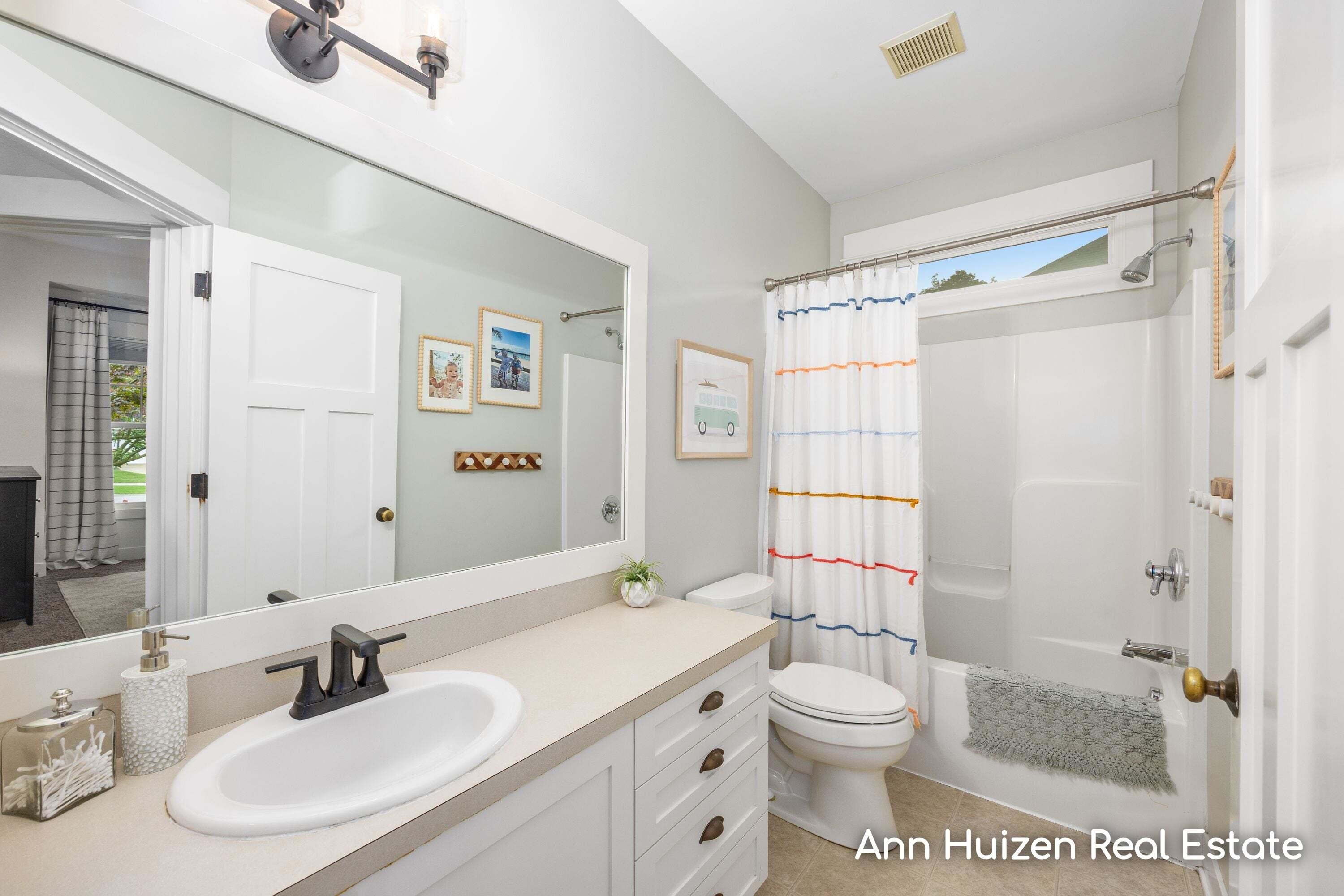 Bathroom with a white vanity and large mirror beside a tub-shower with a colorful striped curtain.
