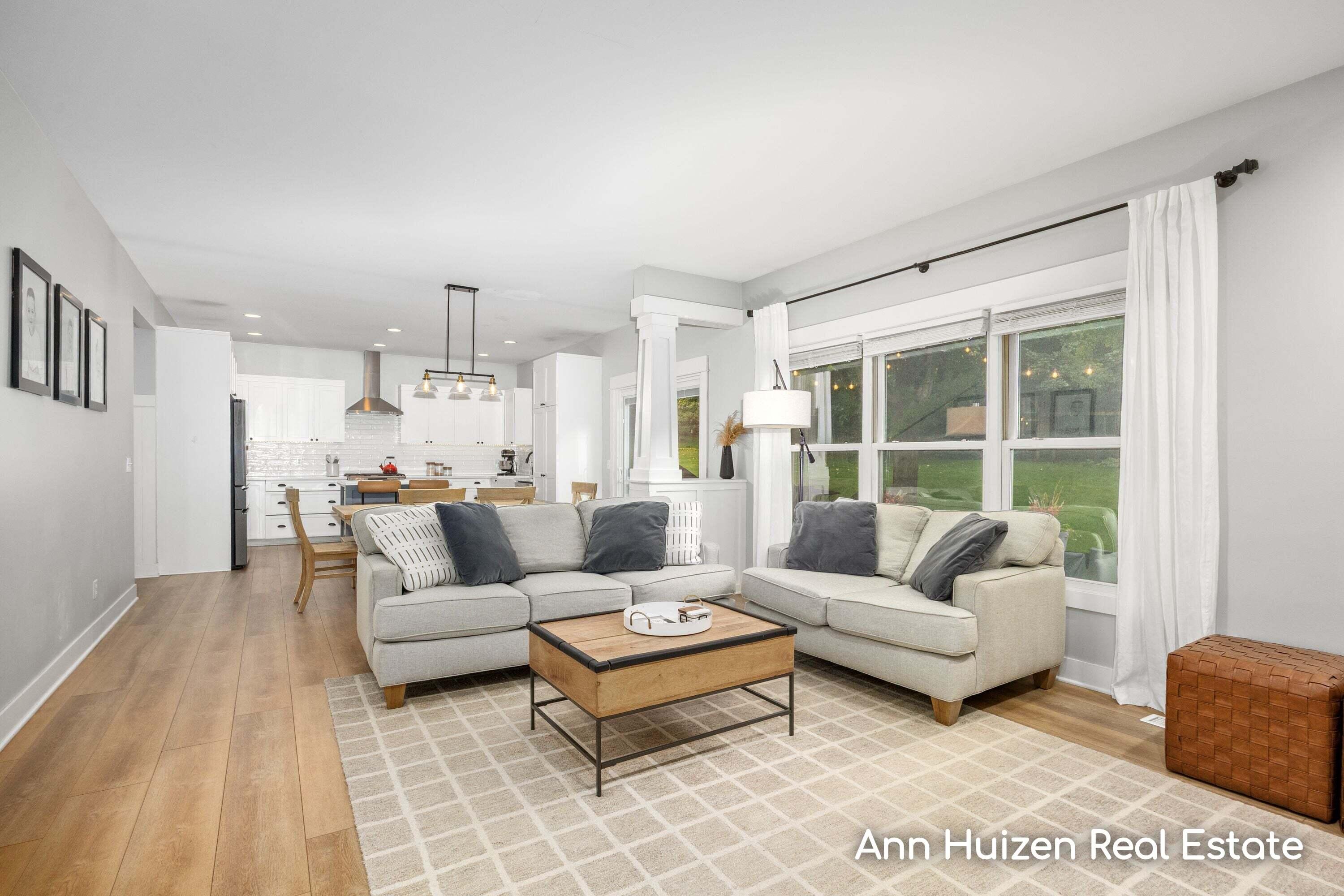 Open-plan living room with light sofas and large windows overlooking a green lawn.