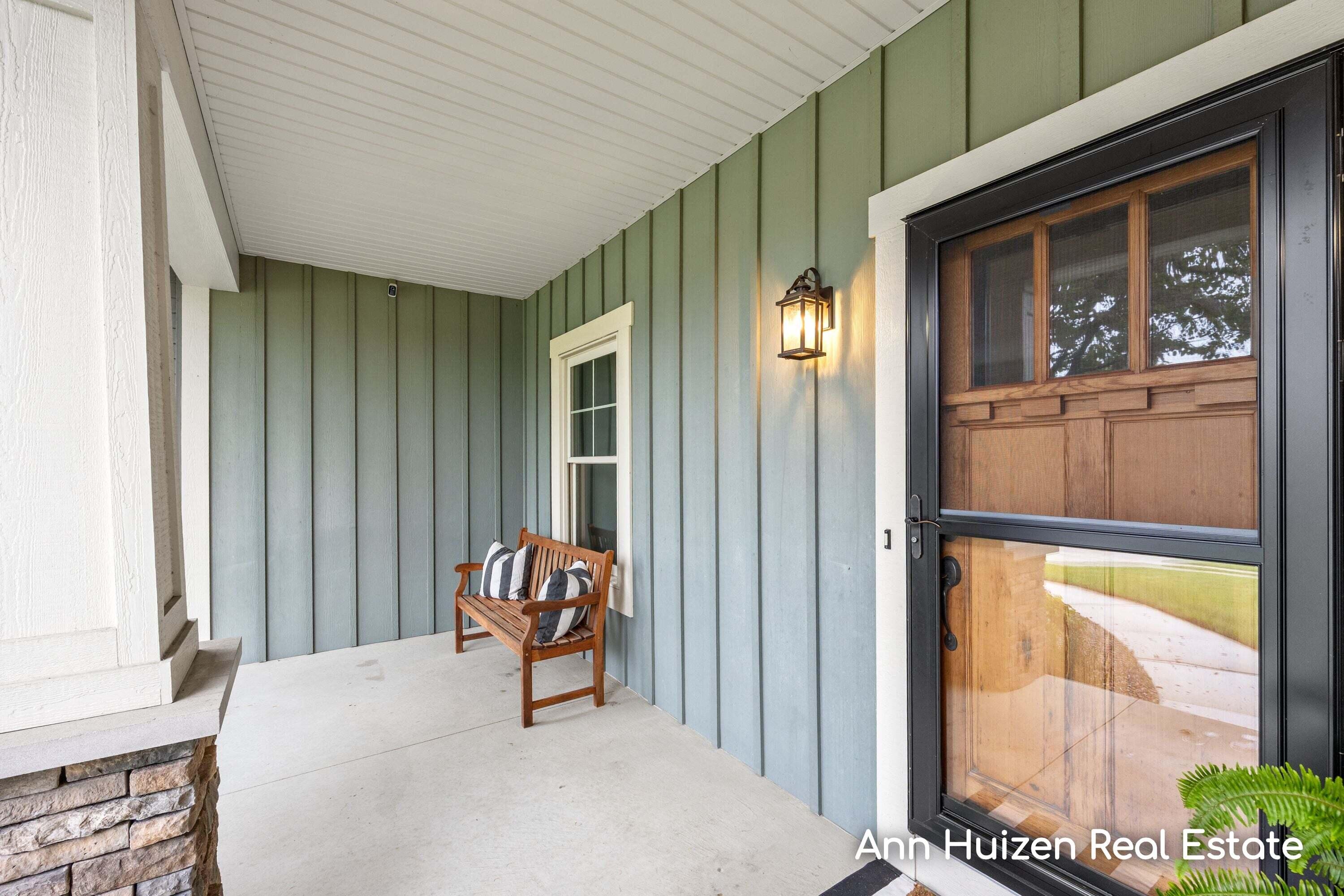 Covered front porch with a wooden bench, blue-green siding, and black-framed glass entry door.