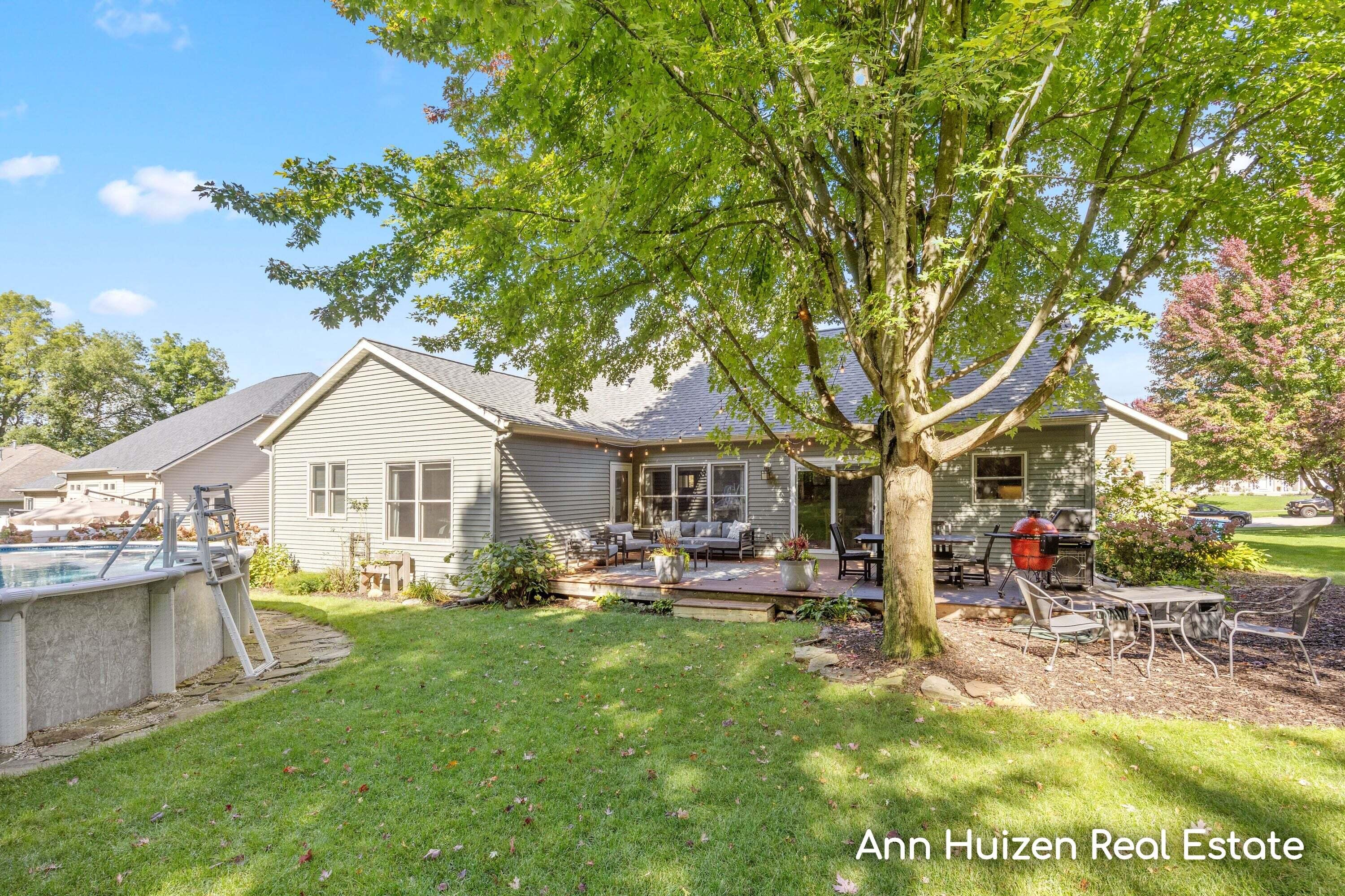 Home’s backyard with a furnished deck, above-ground pool, and patio seating beneath a large tree.