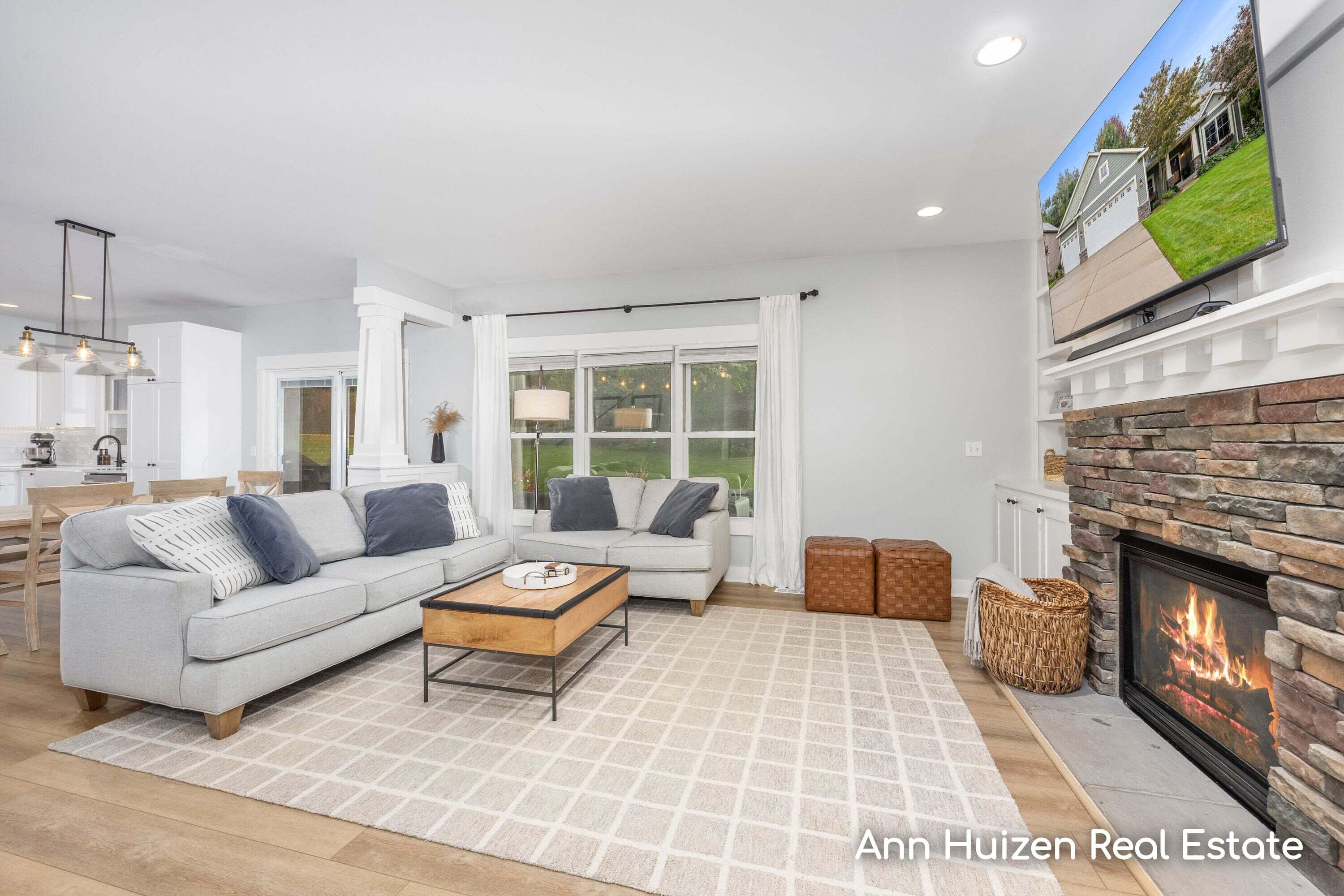 Furnished living room with a gray sectional, stone fireplace, and open kitchen and dining area.