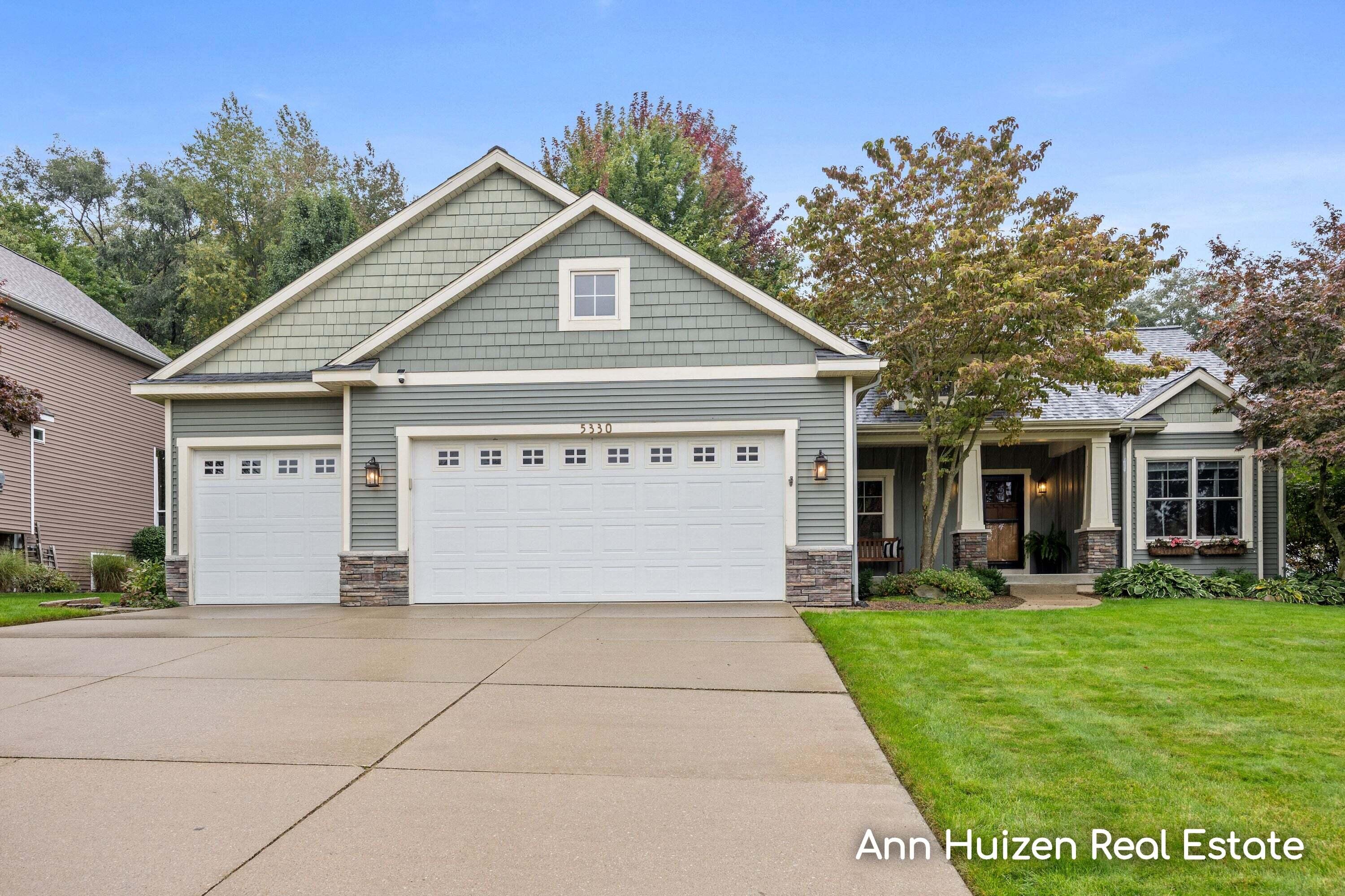 Gray-green home with a three-car garage, stone accents, and a covered front porch.