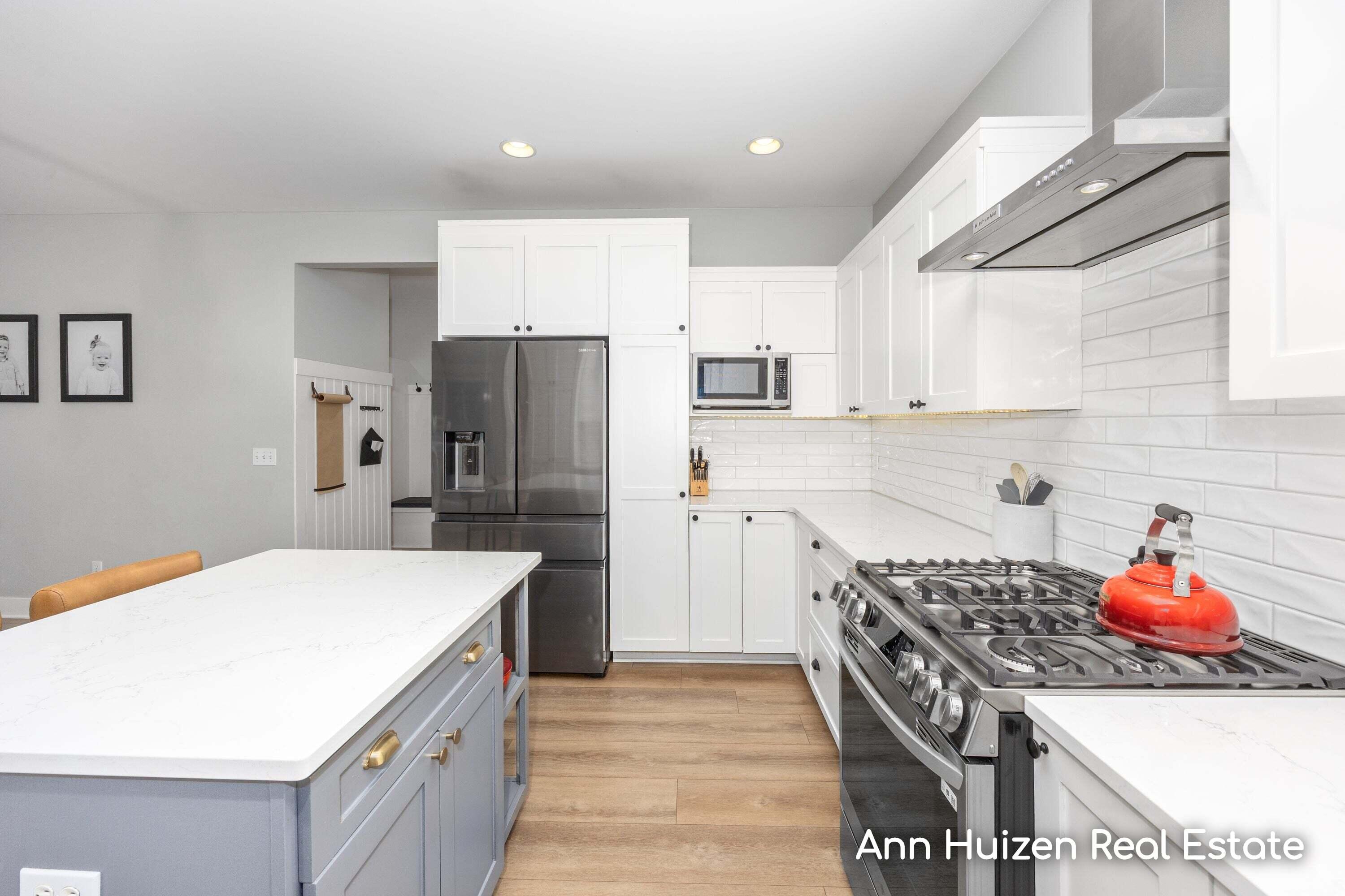Modern kitchen with a large white island, stainless appliances, and a red kettle on the gas range.