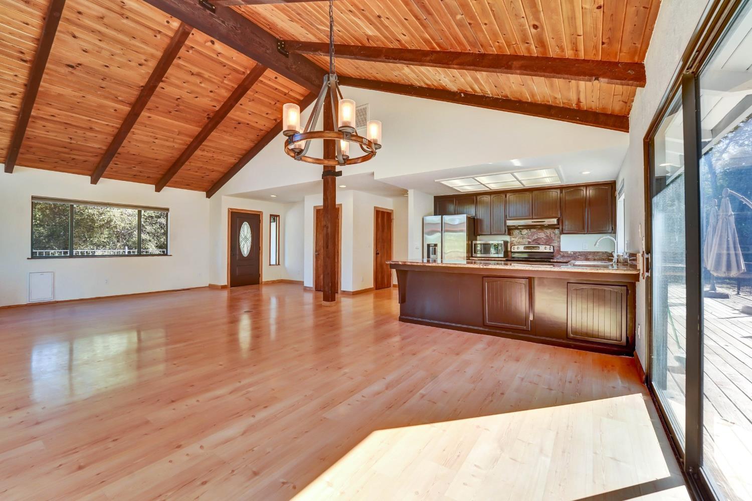 Open living room and kitchen with vaulted wood ceiling, exposed beams, and sliding doors to a deck.