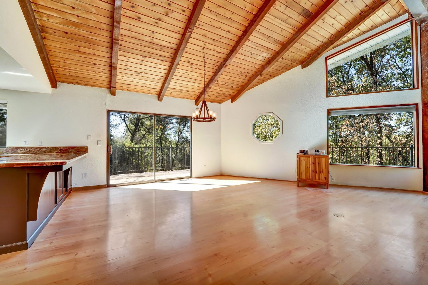 Living room with a vaulted wood ceiling, large tree-view windows, and a sliding door to the deck.
