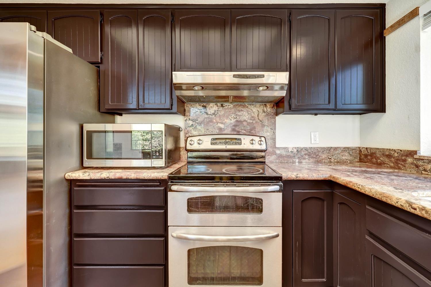 Kitchen with dark cabinetry, stainless steel appliances, and stone-pattern counters and backsplash.