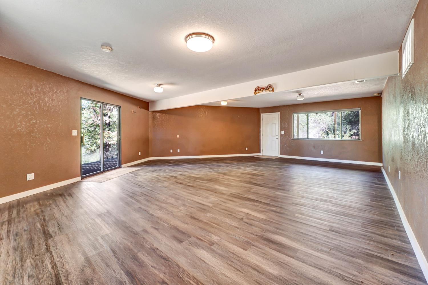Vacant spacious room with wood-look plank flooring, brown walls, and a sliding glass door.