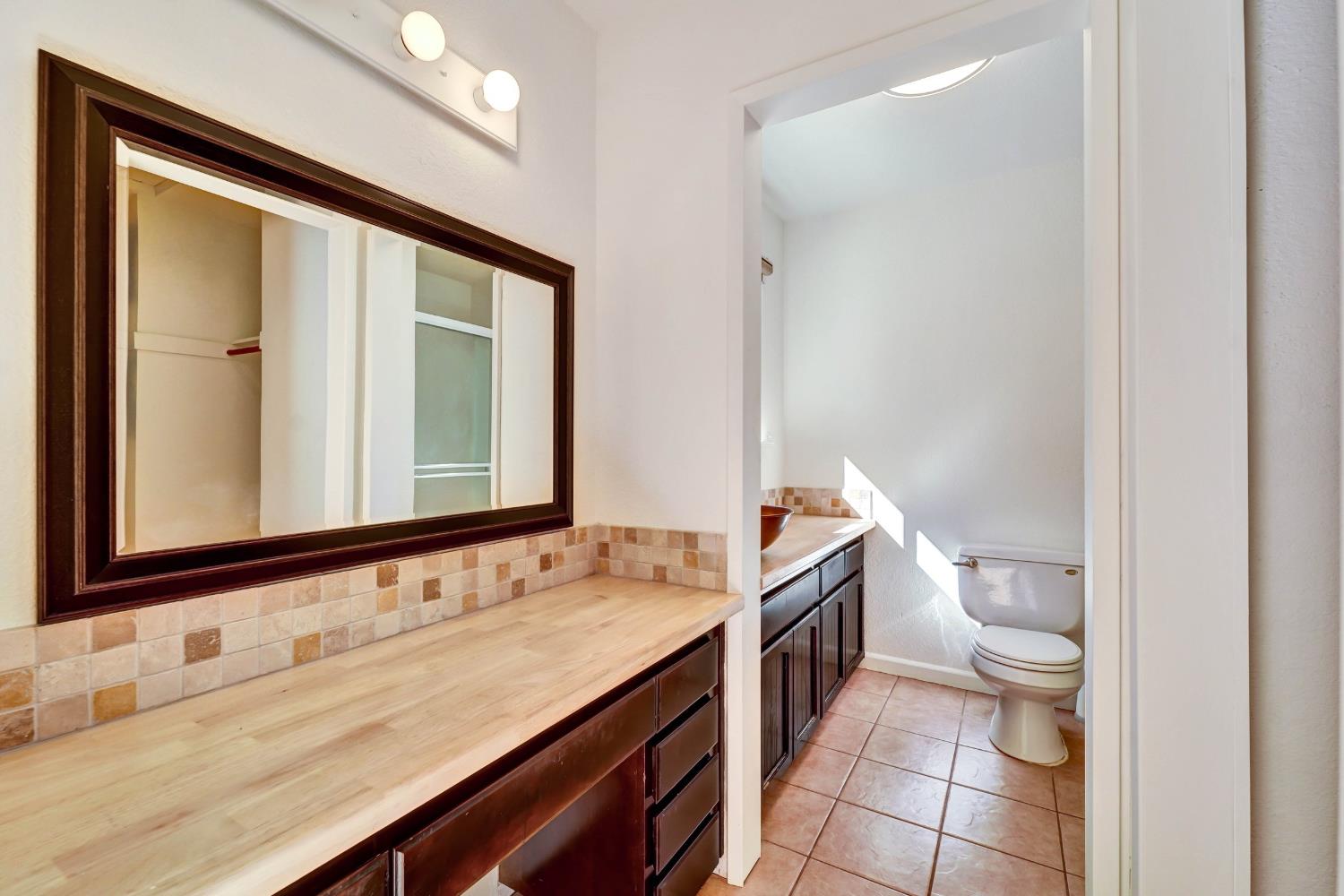 Bathroom vanity with a large framed mirror and tiled backsplash beside a separate toilet area.