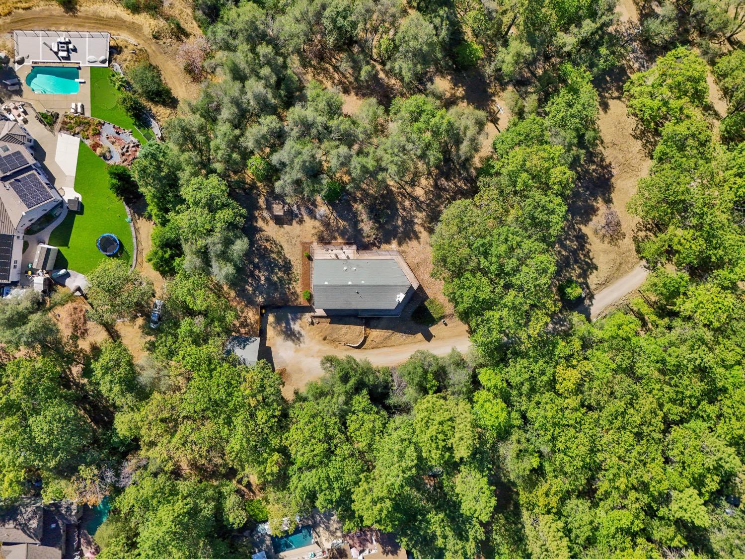 Aerial view of a house among mature trees, with a dirt driveway and wooded surroundings.