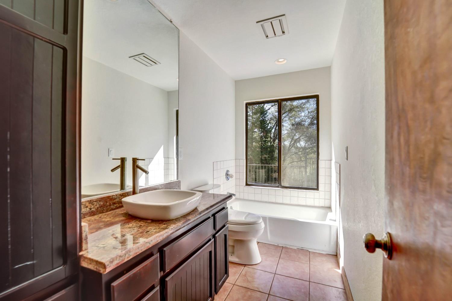 Bathroom with a granite vanity and vessel sink beside a tub under a large window.