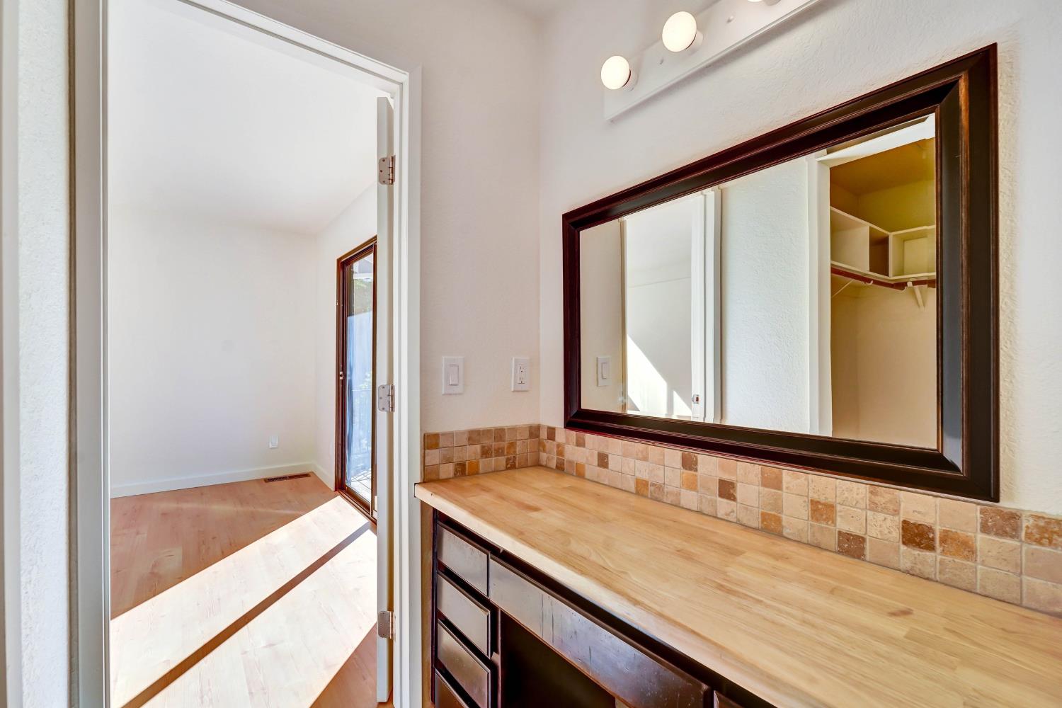 Bathroom vanity with a long wood countertop, tiled backsplash, and dark-framed mirror.