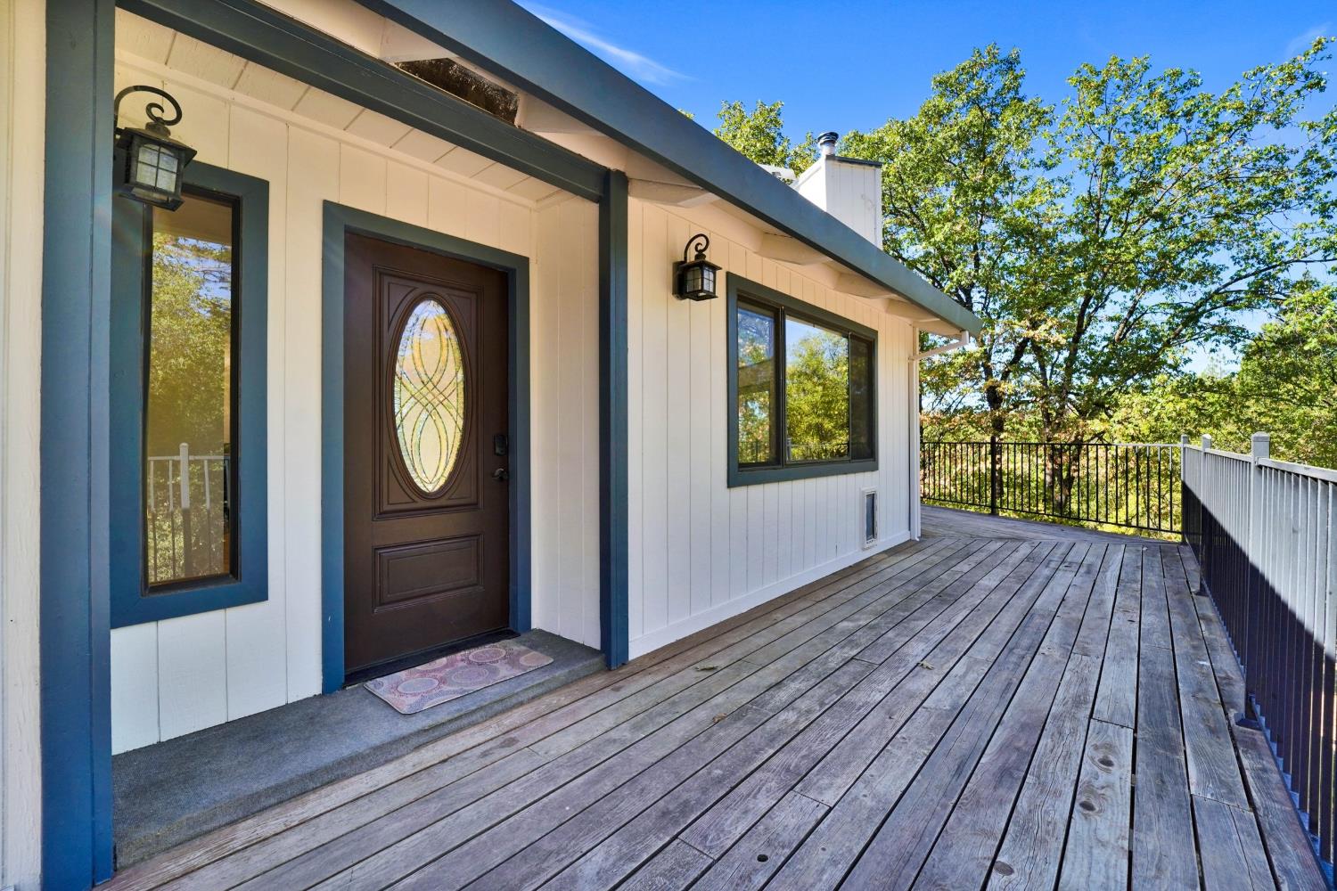 Home entrance with an oval-glass front door opening onto a wide wooden deck bordered by metal railings.