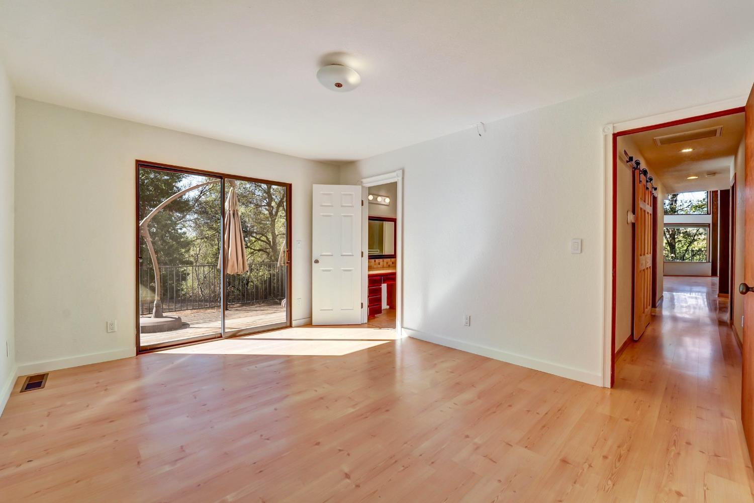 Empty room with light wood floors and sliding glass doors opening onto a wooded deck.