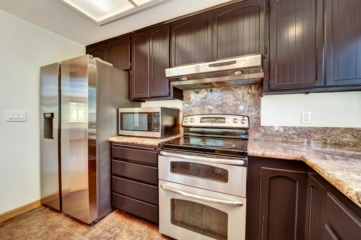 Kitchen with dark cabinets, stainless steel appliances, mottled stone counters, and a ceiling skylight.