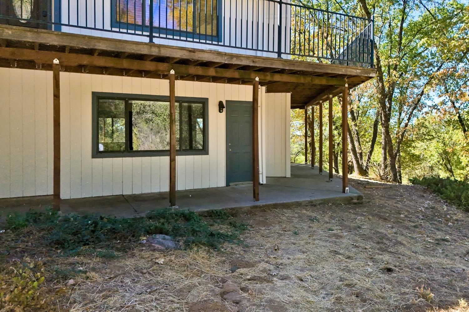 Wooded home exterior with a raised deck and covered patio beneath it.