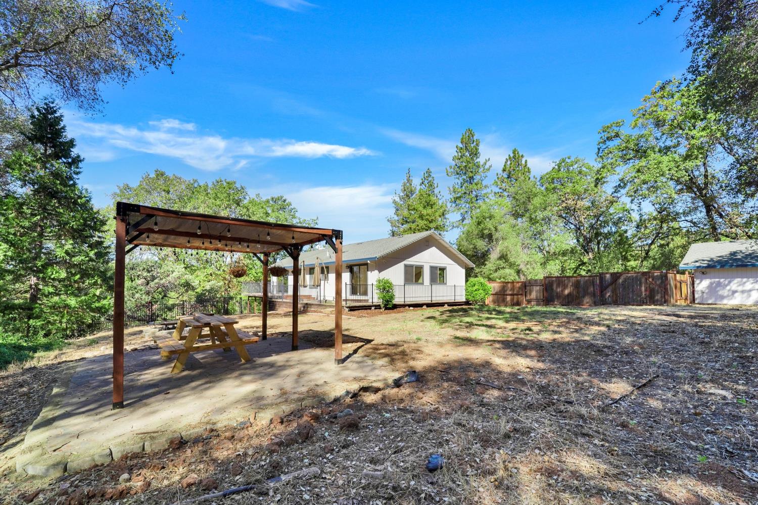 Backyard view of a single-story home with a wooden pergola and picnic table.