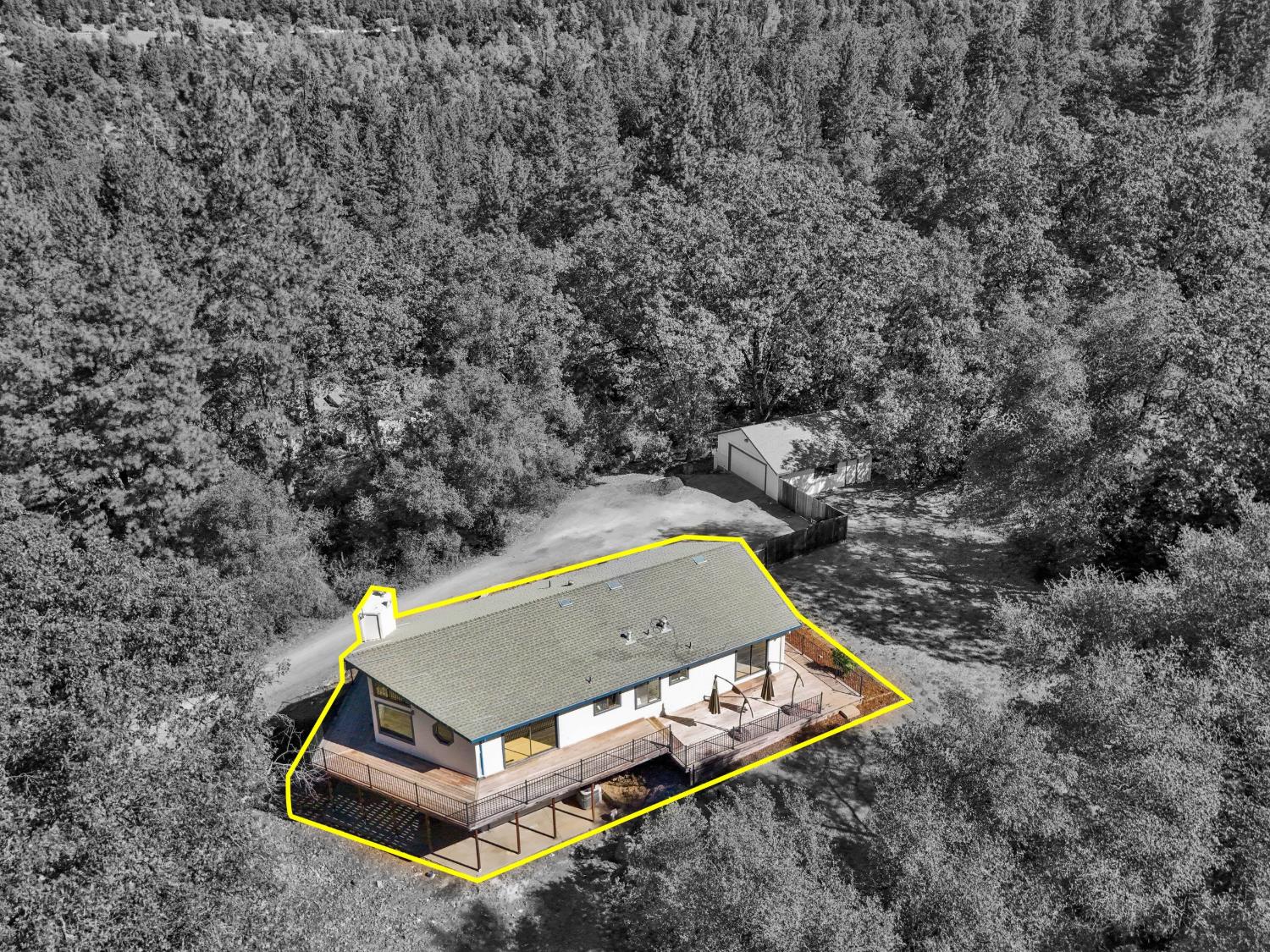 Single-story home with a large raised deck, outlined in yellow amid dense woodland.