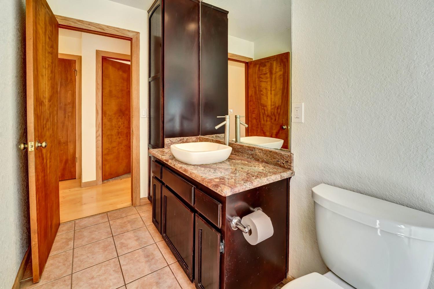 Bathroom vanity with a white vessel sink, stone countertop, large mirror, and toilet.