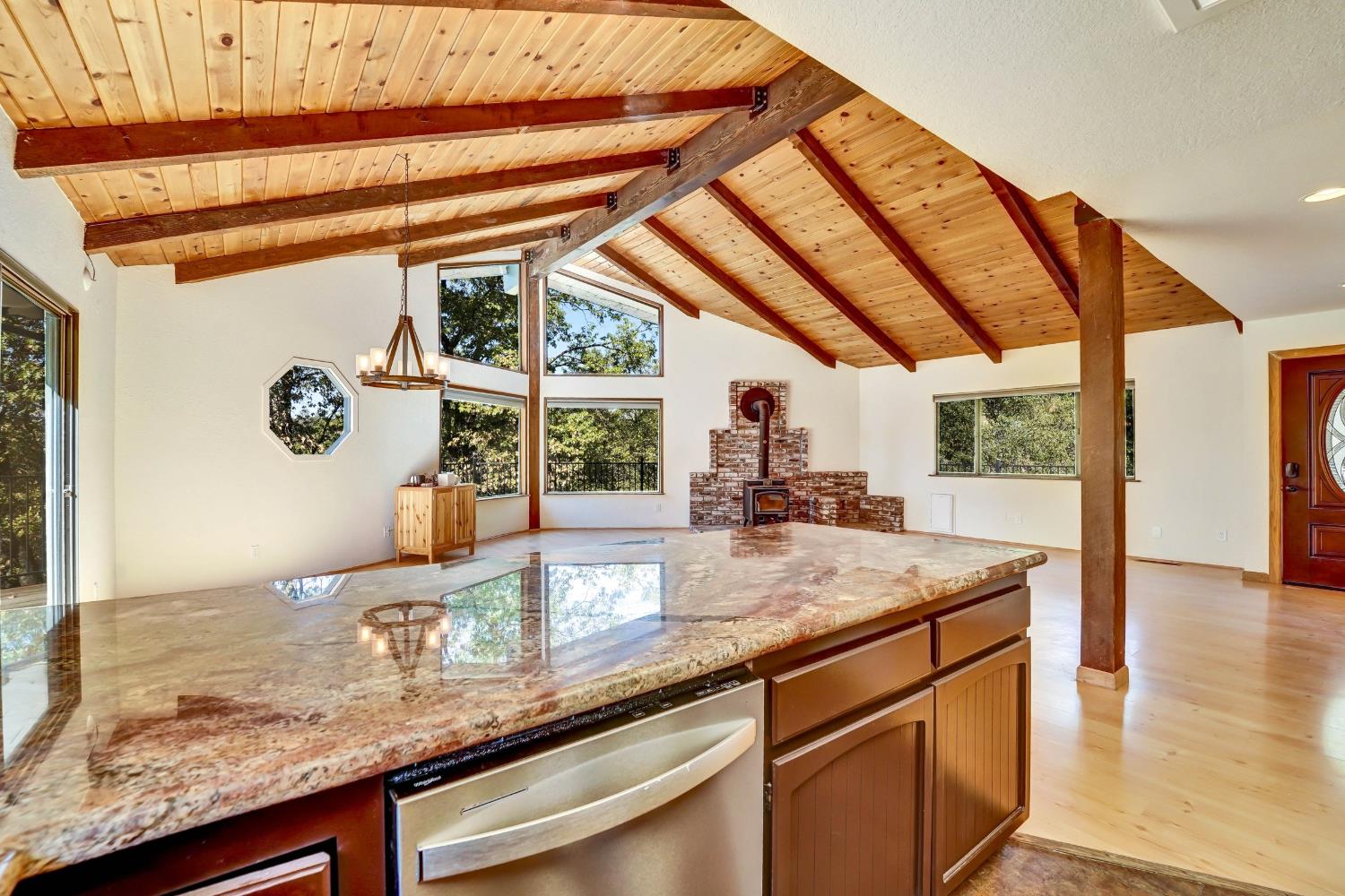 Kitchen with a granite island, vaulted wood ceiling, exposed beams, and brick wood-stove hearth.